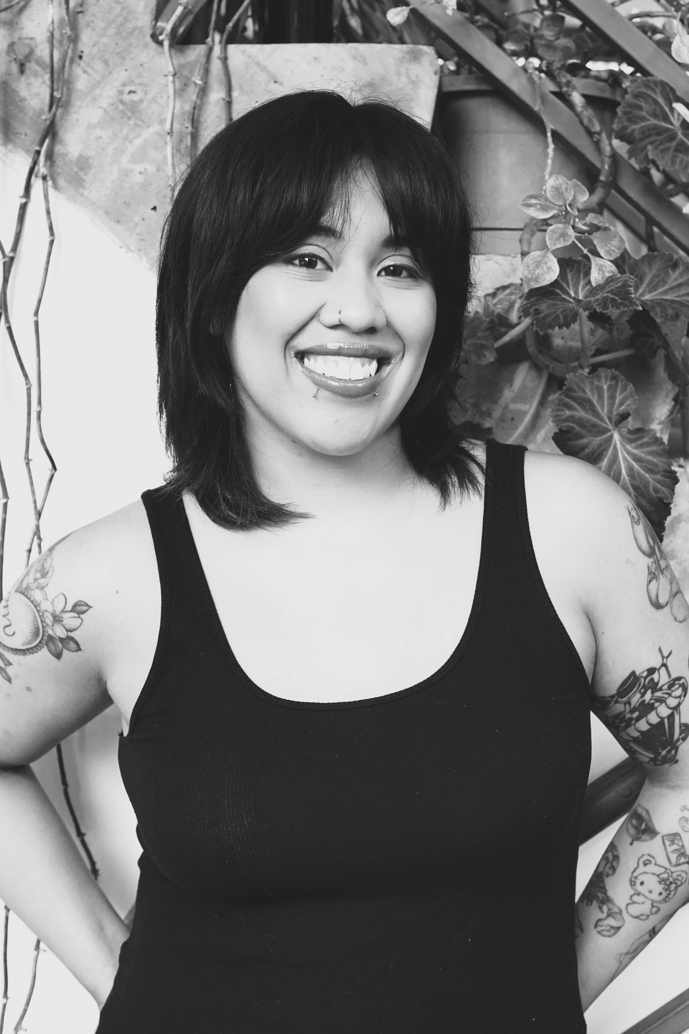 Blow dry specialist at Gem House Salon in Greenpoint, Brooklyn, offering luxury blowout services for Greenpoint and Williamsburg clients, styled hair, arm tattoos, modern piercings, and a black sleeveless top in a plant-filled setting.