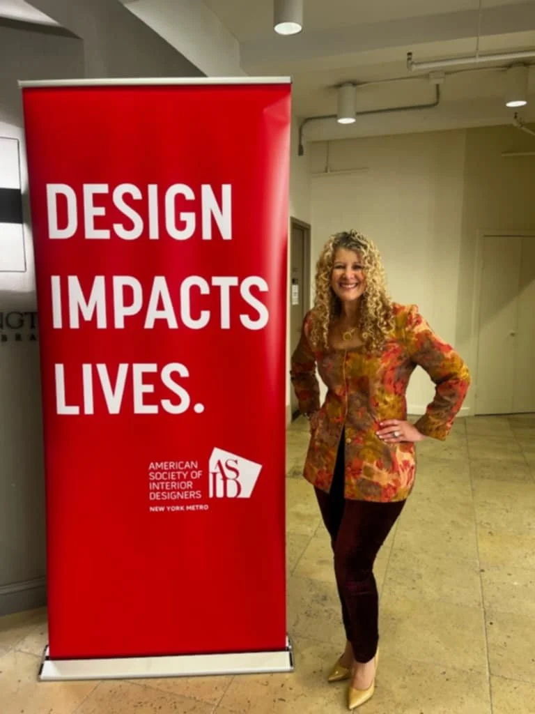 Woman standing next to a red banner that says "Design Impacts Lives" and features the logo of the American Society of Interior Designers, New York Metro.