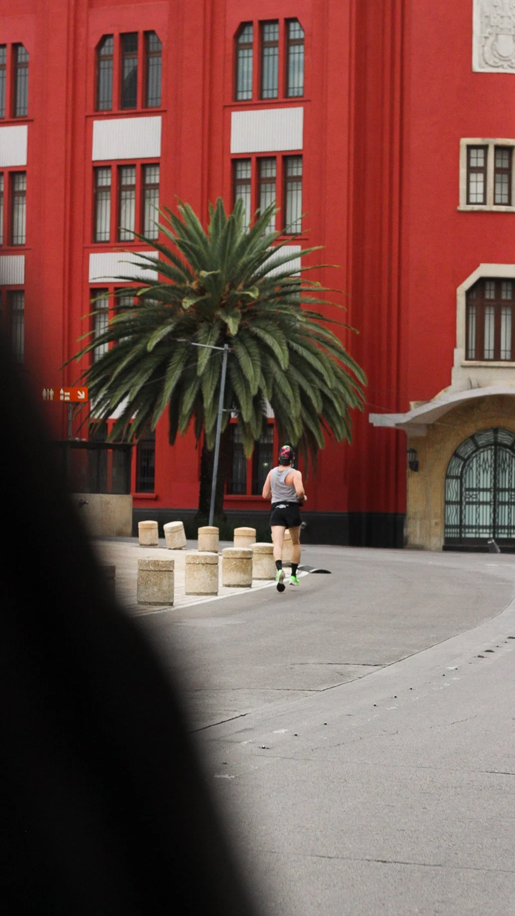 Una persona corriendo en la calle, con un árbol grande y una edificación de color rojo en el fondo.