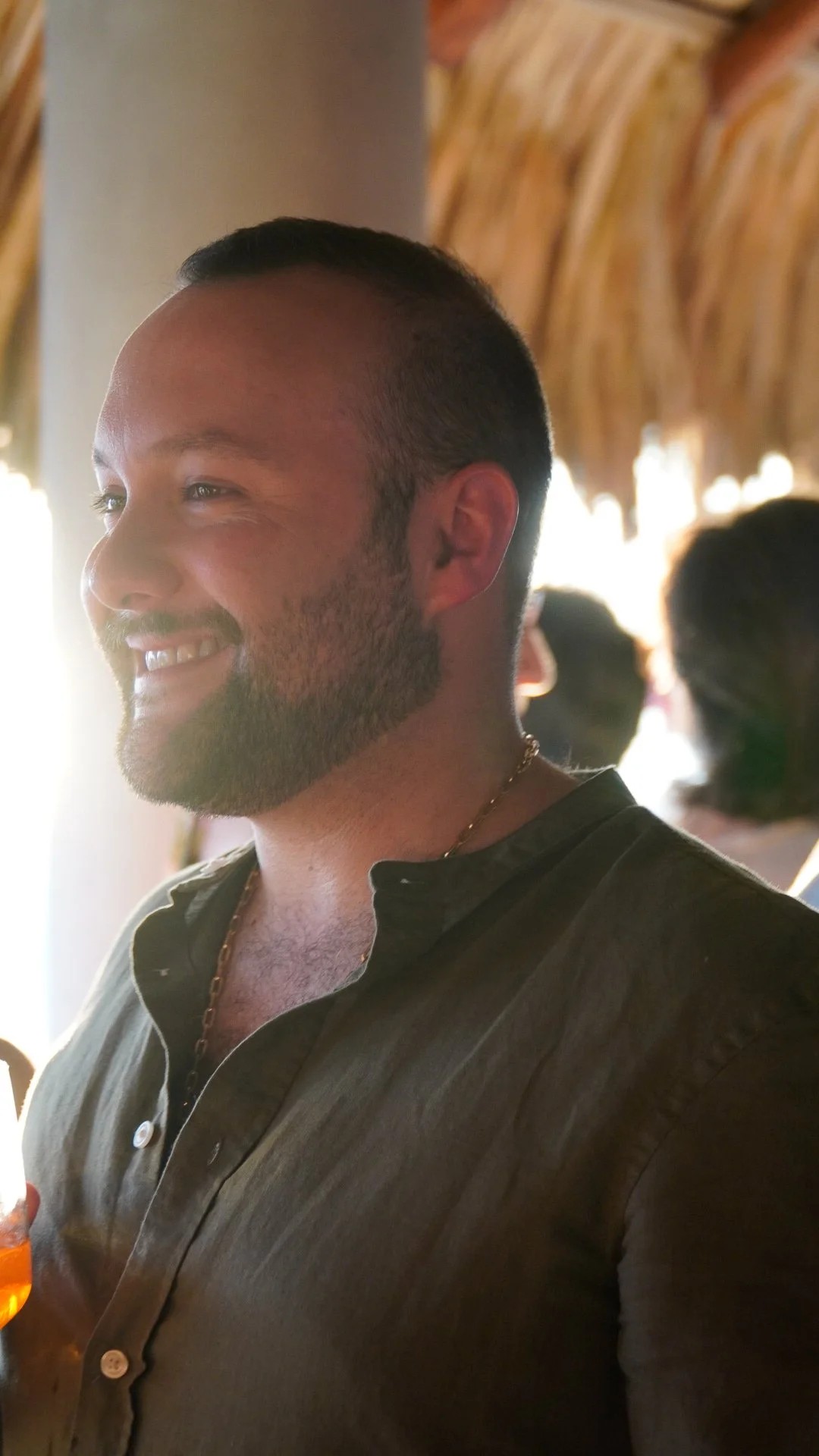 Hombre sonriendo en un lugar con luz natural y fondo de palapa de madera