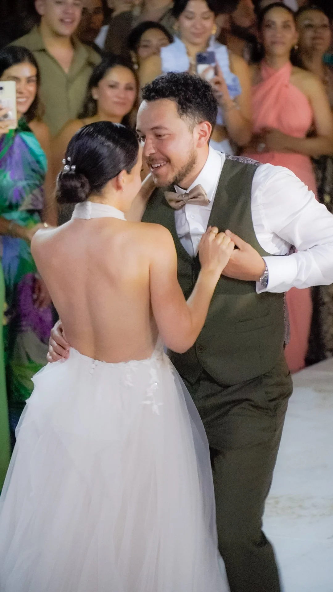 Pareja bailando en su boda, rodeados de amigos y familiares, fondo de gente sonriendo y tomando fotos.
