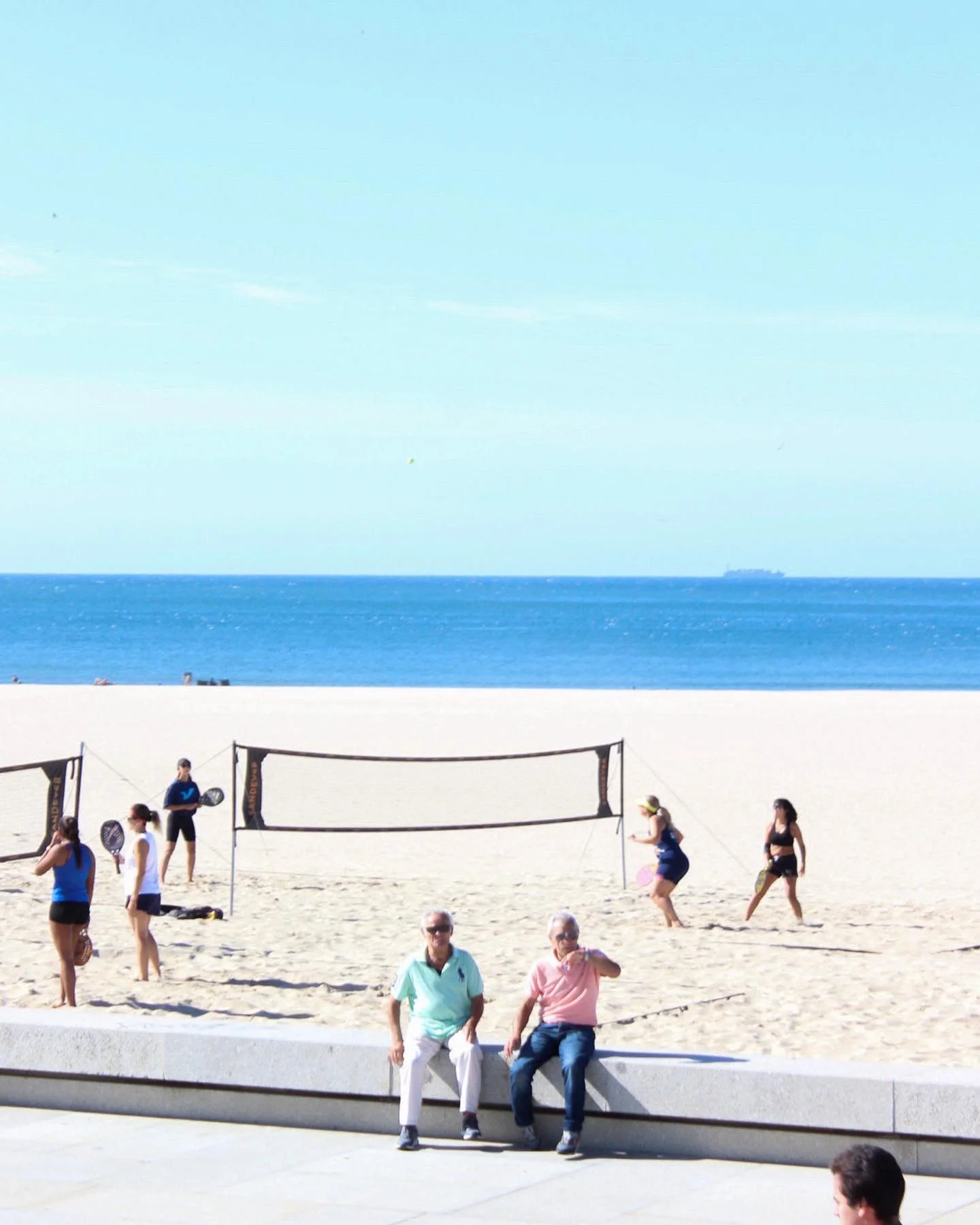 Personas jugando voleibol en la playa, con el mar y el cielo de fondo.