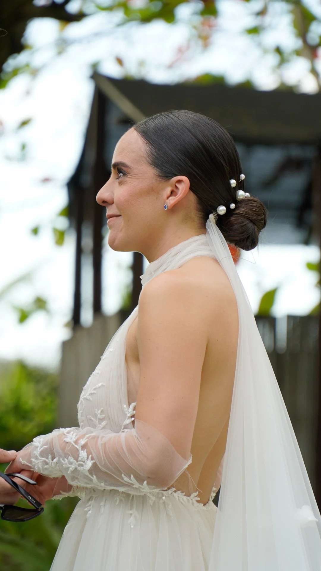 Mujer con vestido de novia y peinado con perlas en un entorno al aire libre.