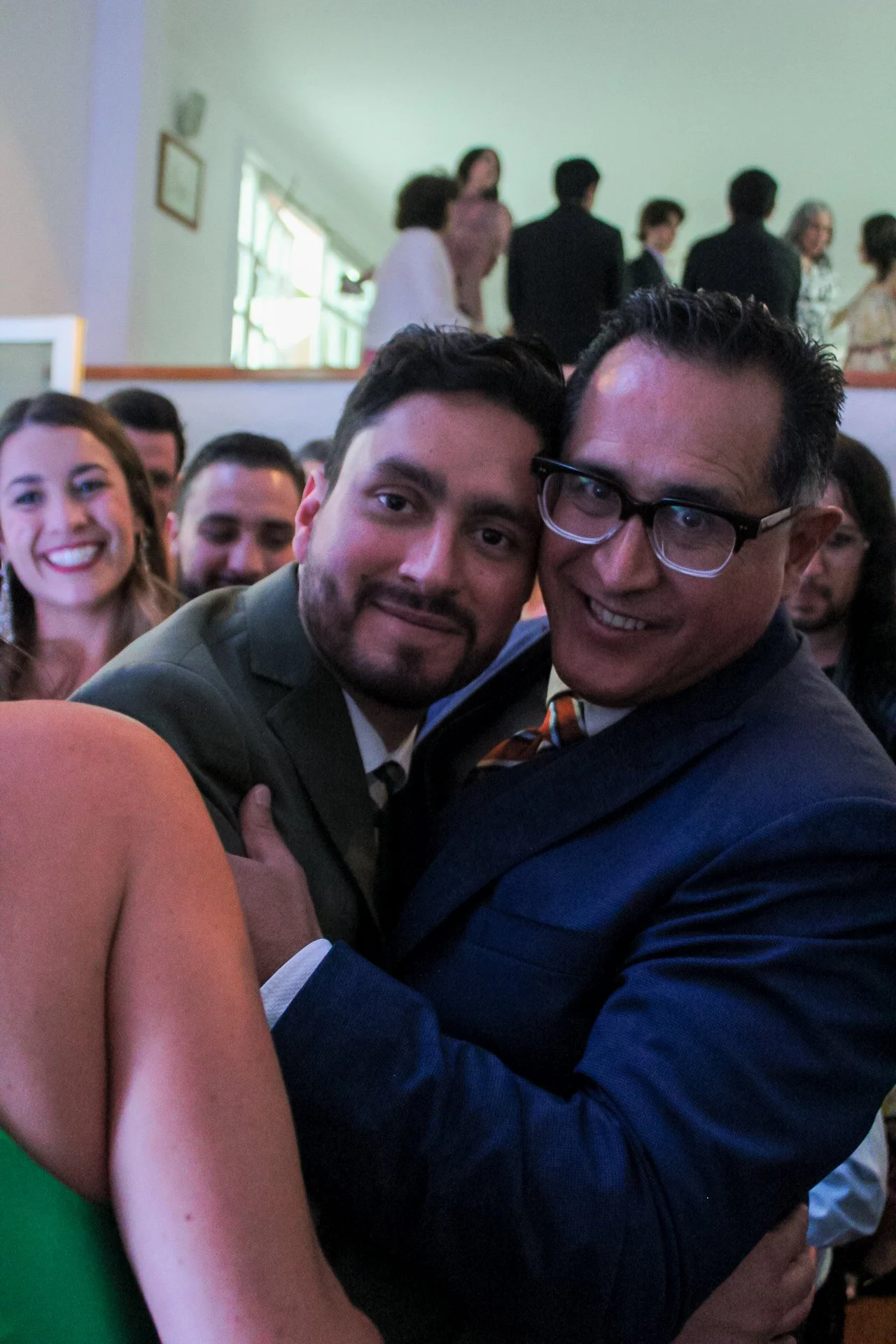 Grupo de personas abrazándose en una celebración. En primer plano, dos hombres son los principales, uno con gafas y el otro con barba, rodeados de otras personas sonriendo.
