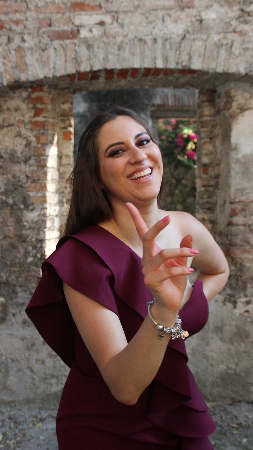 Joven mujer sonriendo y haciendo una señal de paz con la mano en un fondo de paredes de ladrillo expuesto.