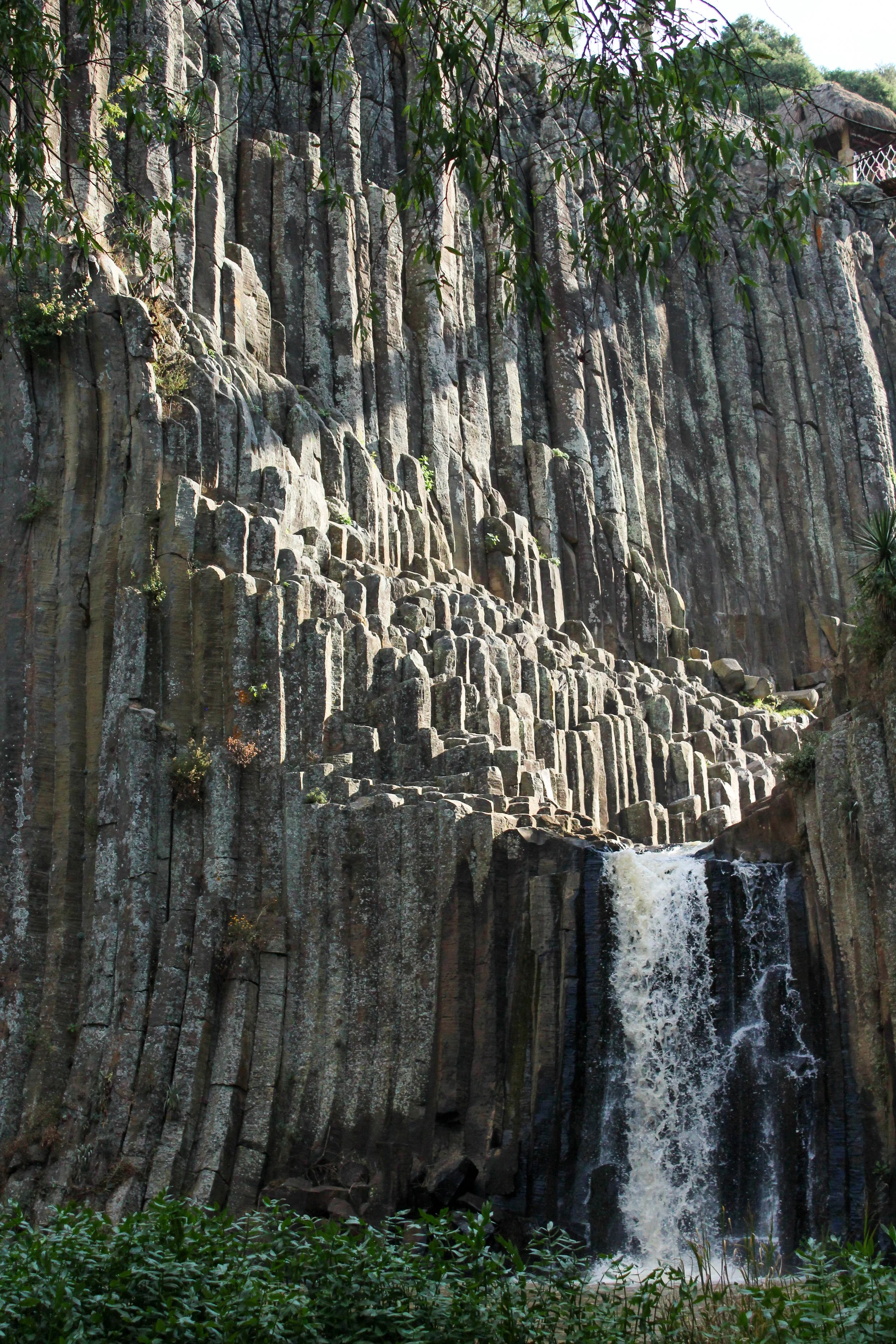 Cascada en un cañón con formaciones rocosas verticales y vegetación en primer plano.