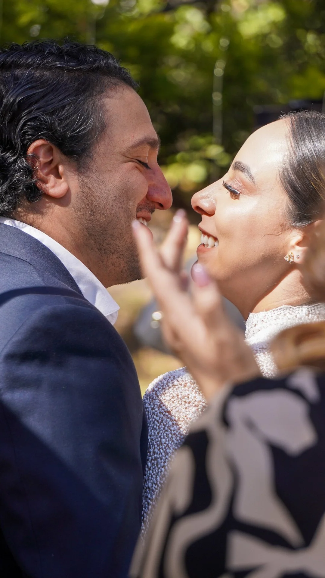 Una pareja sonriendo cara a cara en un entorno natural con árboles verdes al fondo.