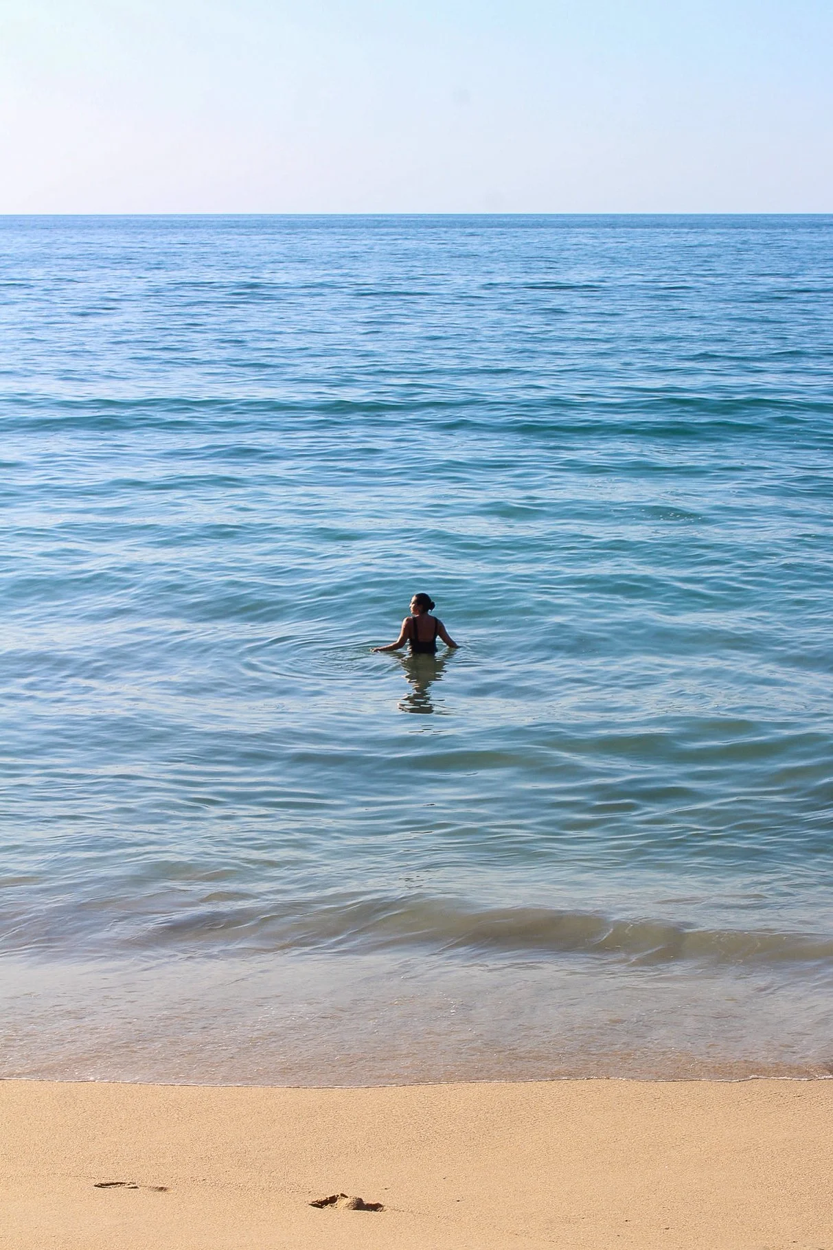 Una mujer nadando en el mar junto a la playa, con aguas tranquilas y arena dorada.