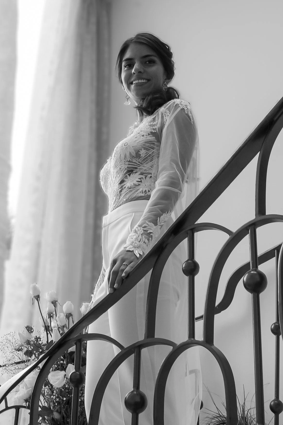 Mujer sonriendo en una escala, vestida con un vestido elegante, en blanco y negro.