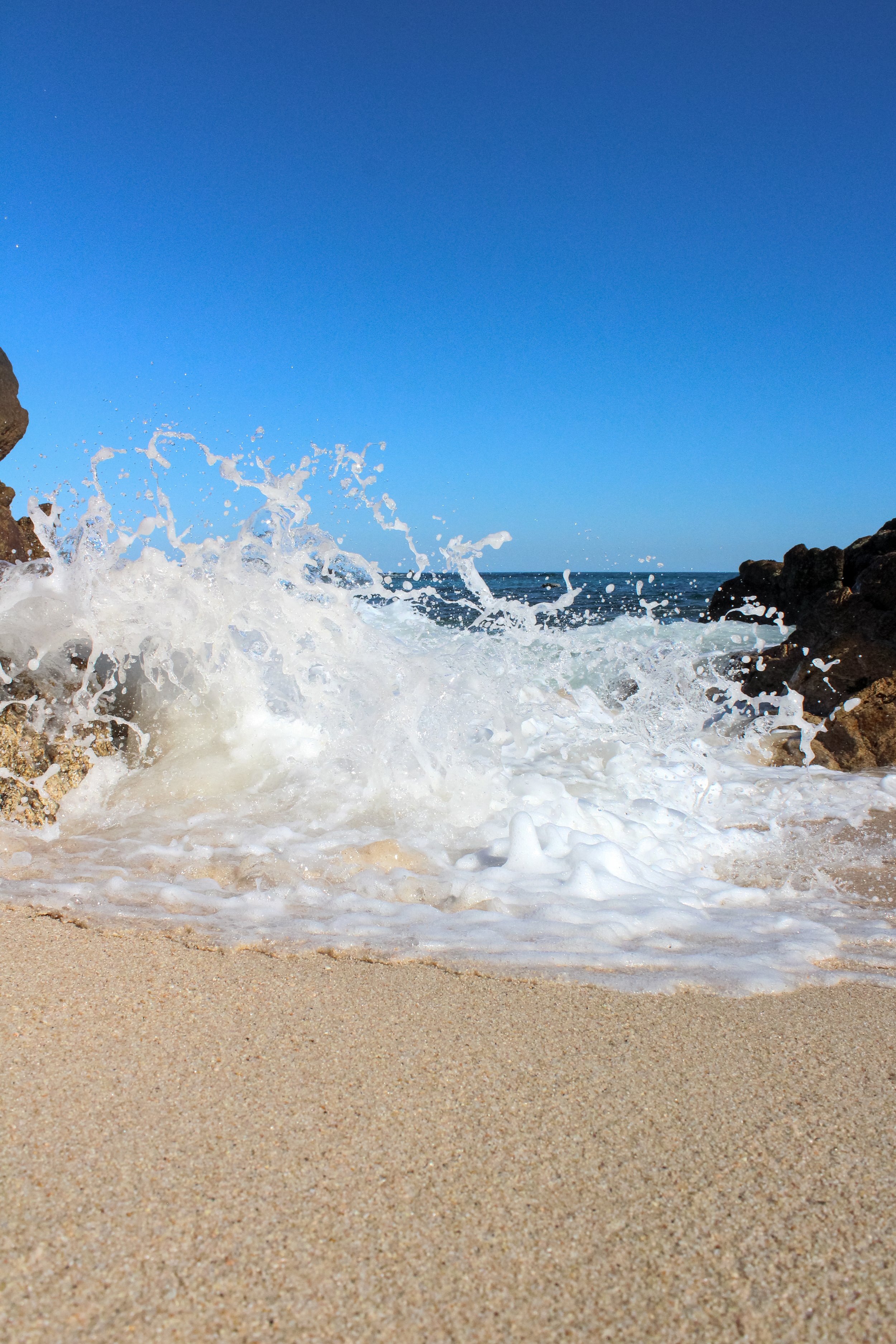 Olas rompiendo en la orilla de una playa de arena con rocas, bajo un cielo despejado