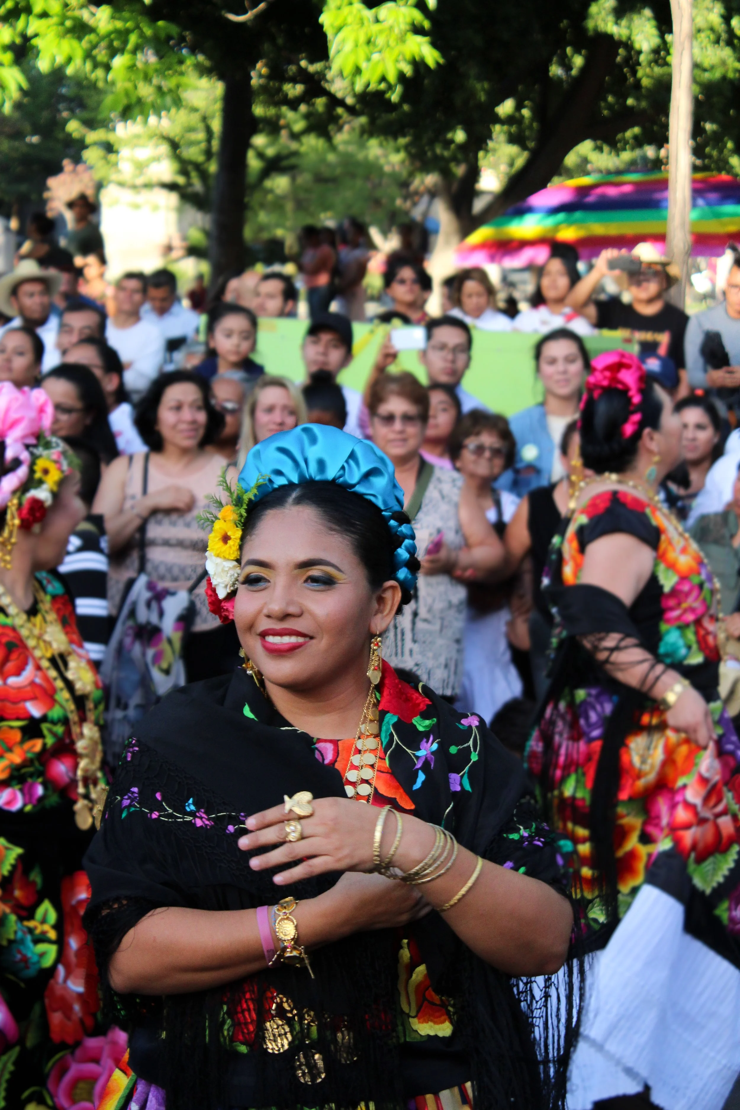 Mujeres vestidas con ropa tradicional mexicana, realizando un baile en una celebración al aire libre con un grupo de personas que observan.