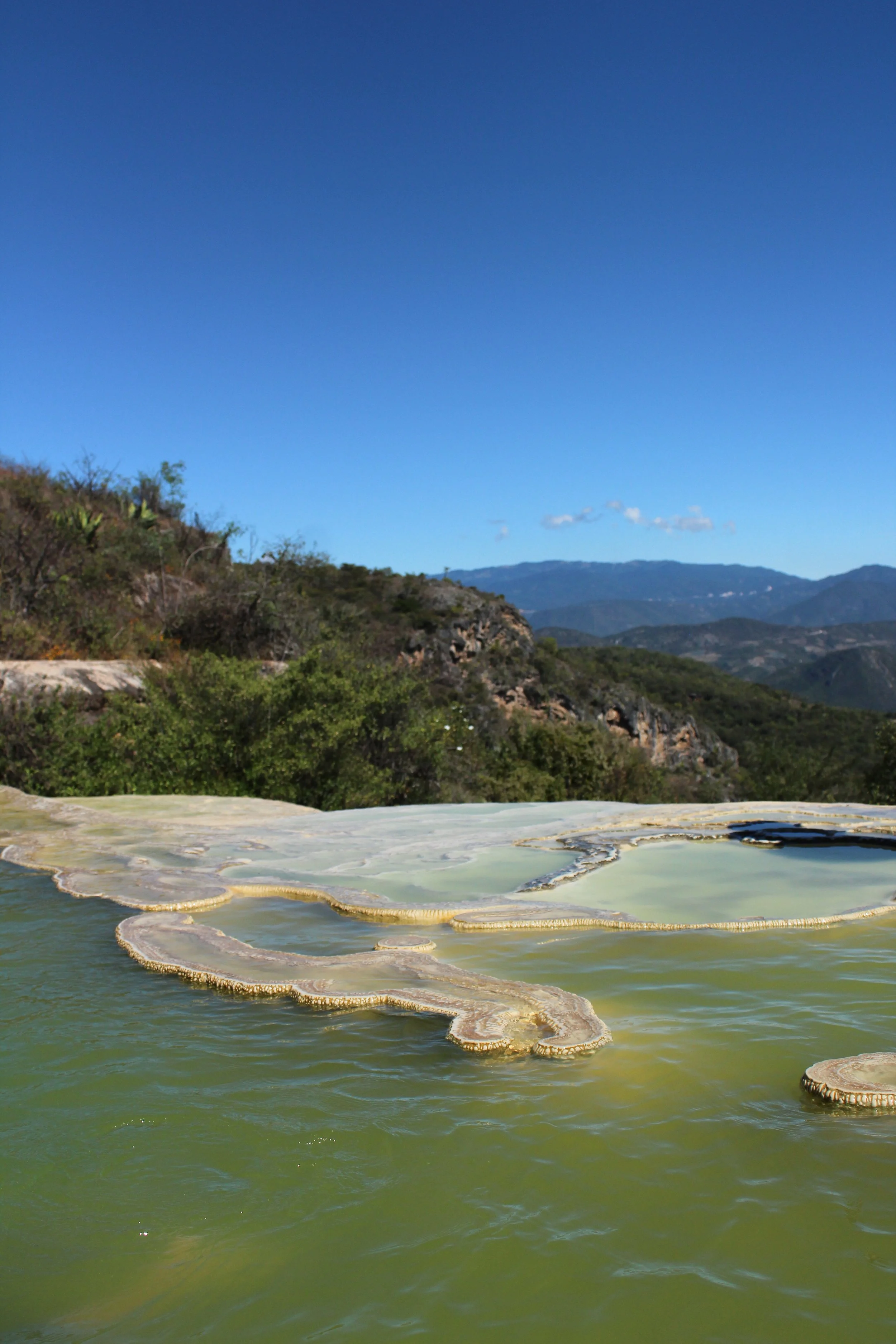 Pantano con depósitos minerales en una zona montañosa bajo un cielo despejado.