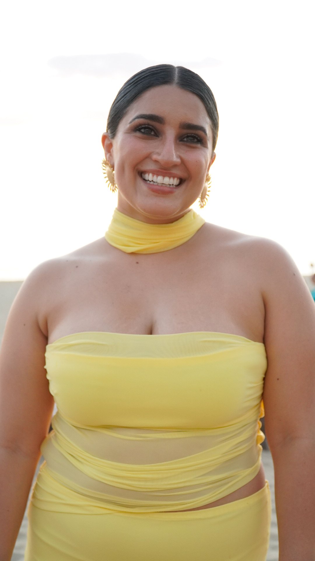 Mujer sonriendo con vestido amarillo en un entorno al aire libre.
