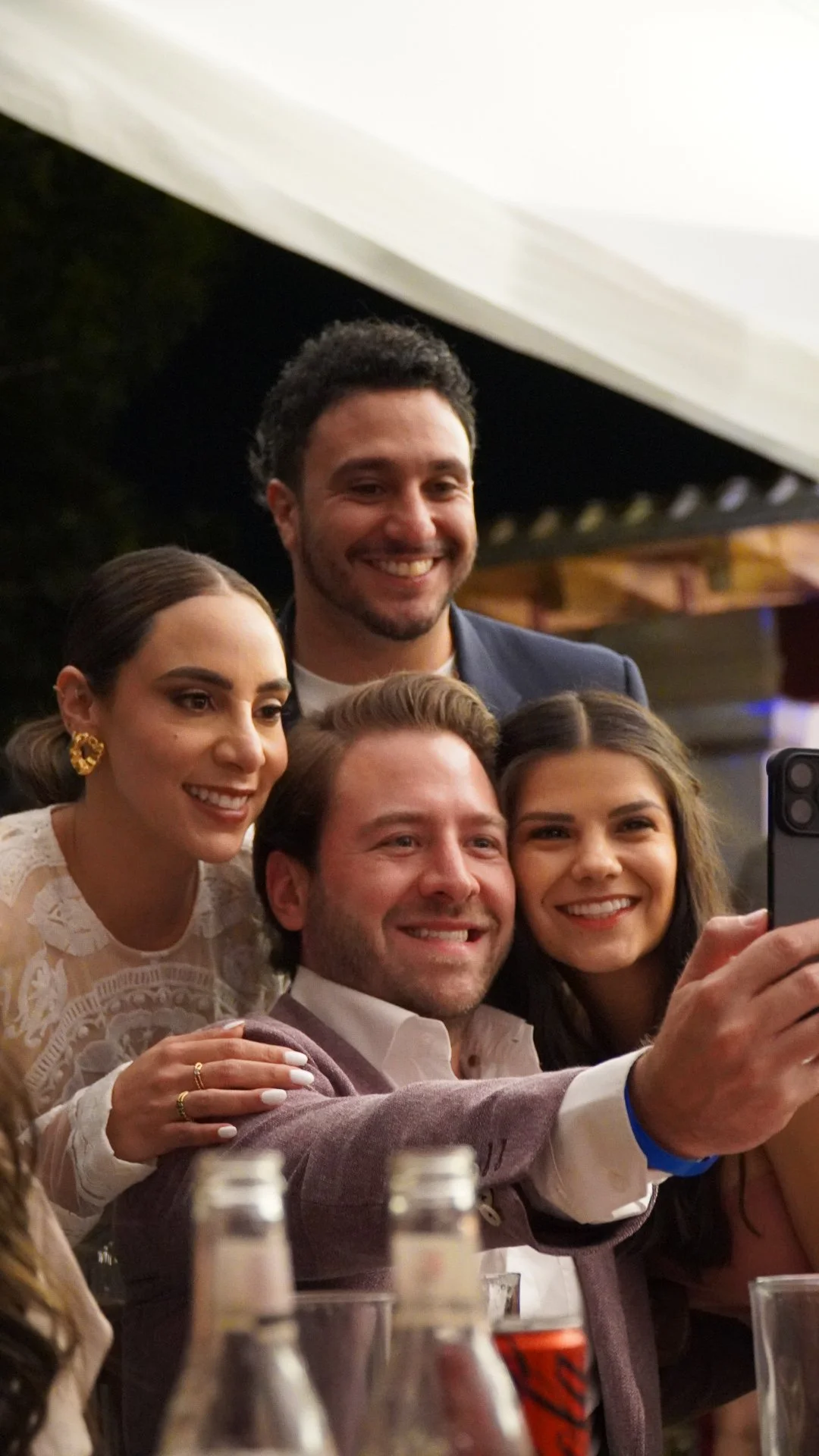 Grupo de cinco personas sonriendo y tomando una selfie en una reunión social.