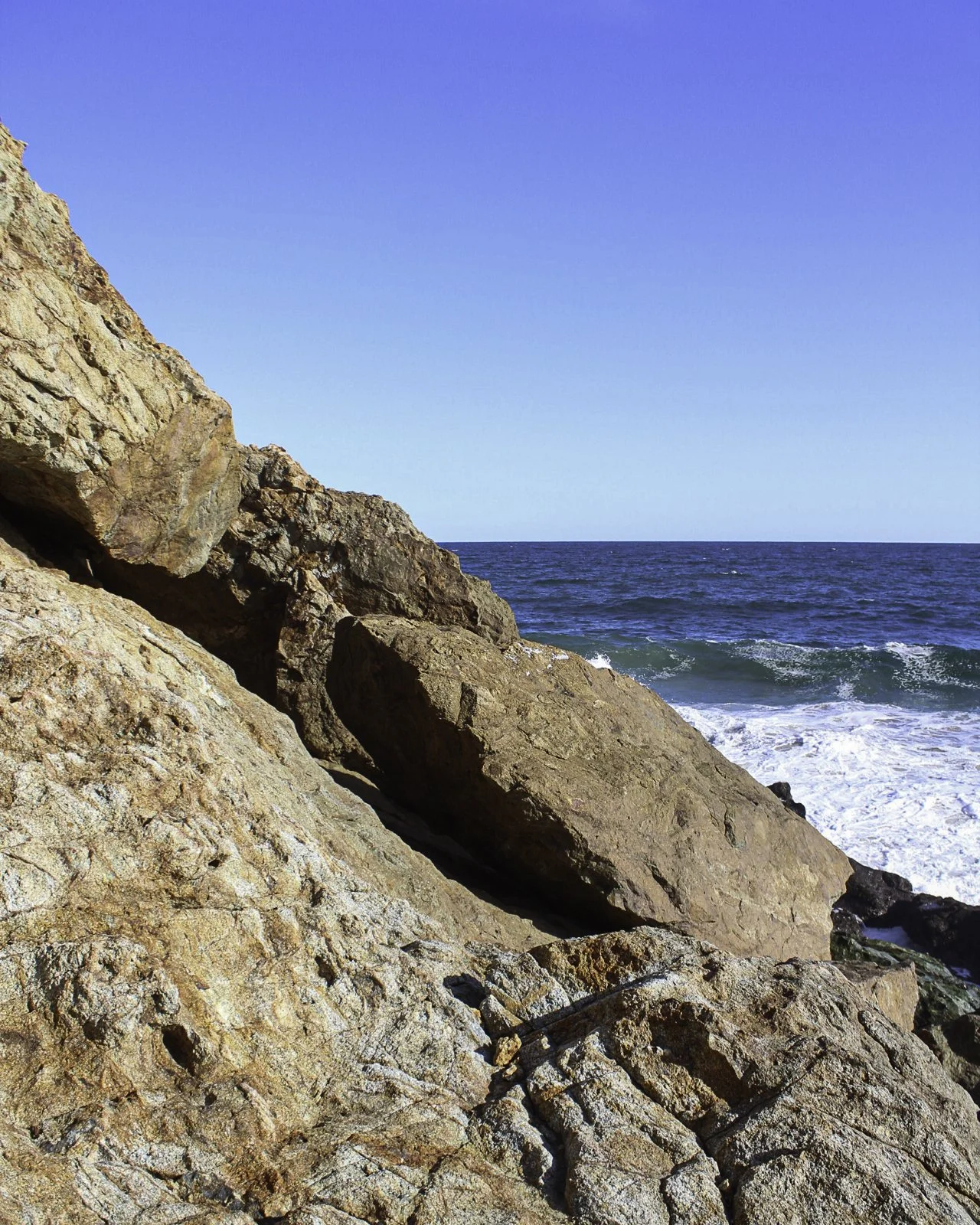 Rocas en la costa con el mar y el cielo azul en el fondo.