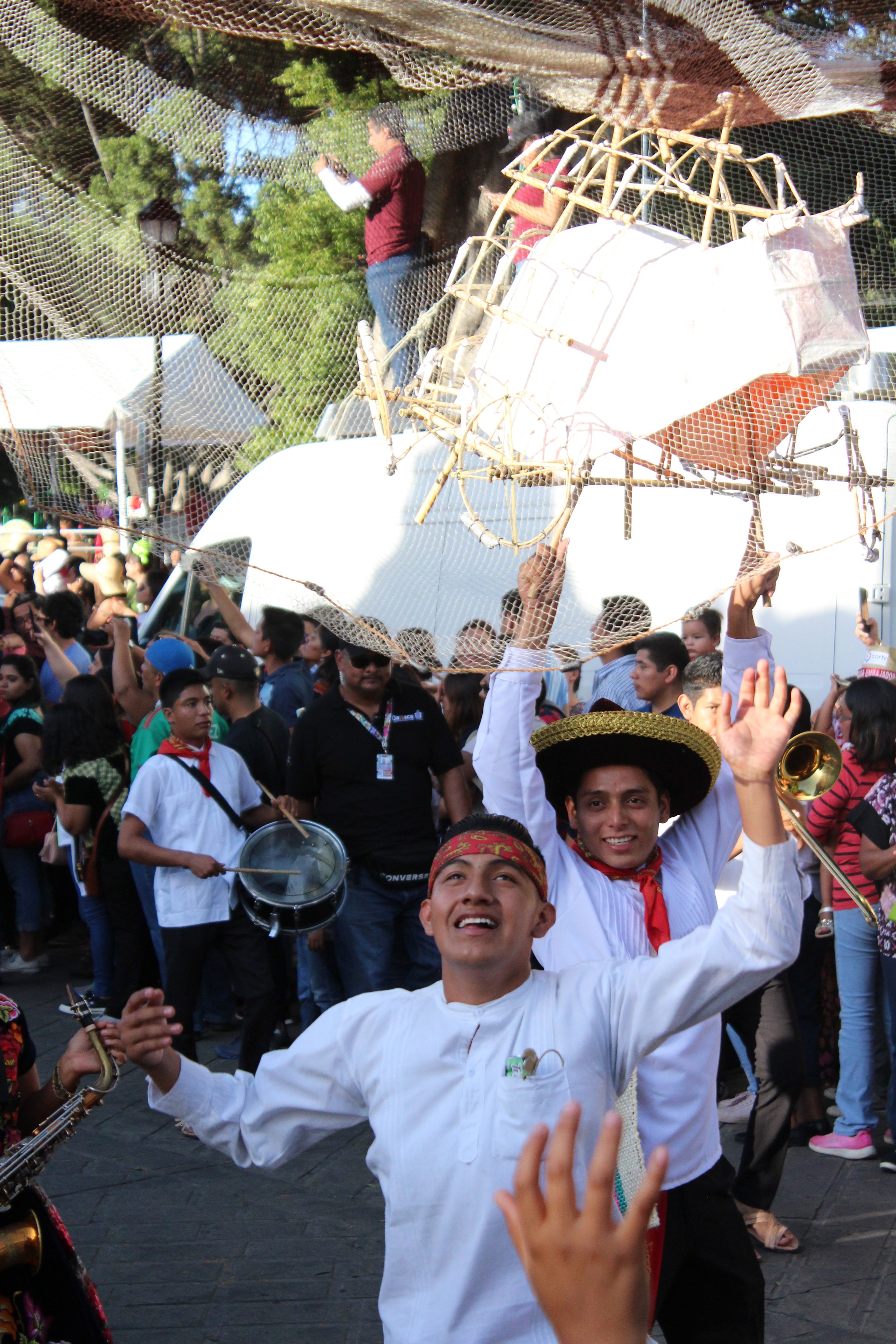 Personas bailando y tocando instrumentos en una festividad con un ambiente alegre, con un carro alegórico decorado y un grupo de personas en un evento al aire libre.