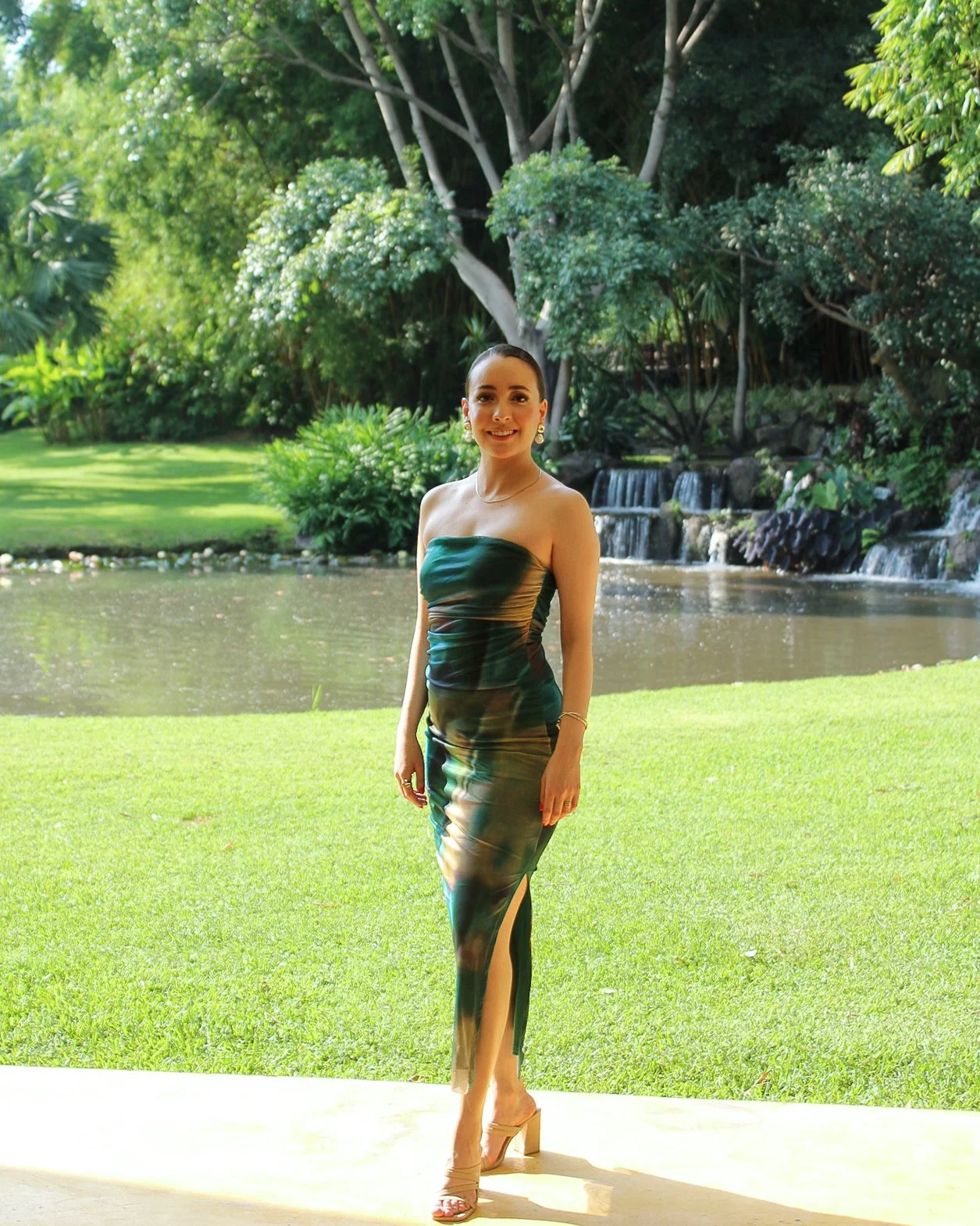 Mujer con vestido largo sentado en un jardín con fuente y árboles