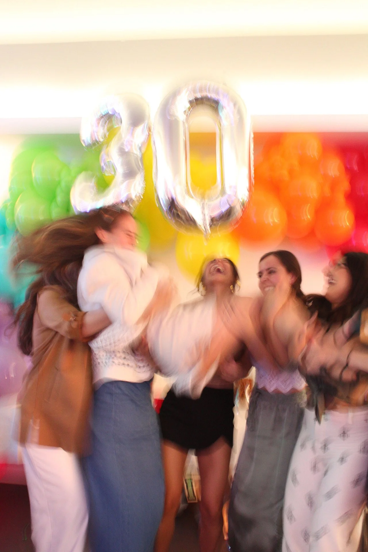Grupo de mujeres celebrando con globos en forma de números 30, rodeadas de globos de colores.
