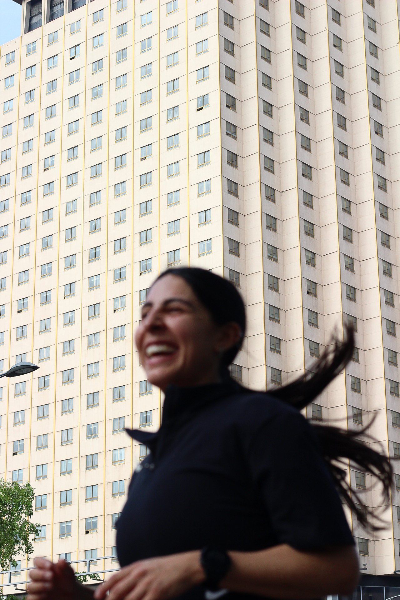 Una mujer corriendo y sonriendo con un edificio alto de fondo.