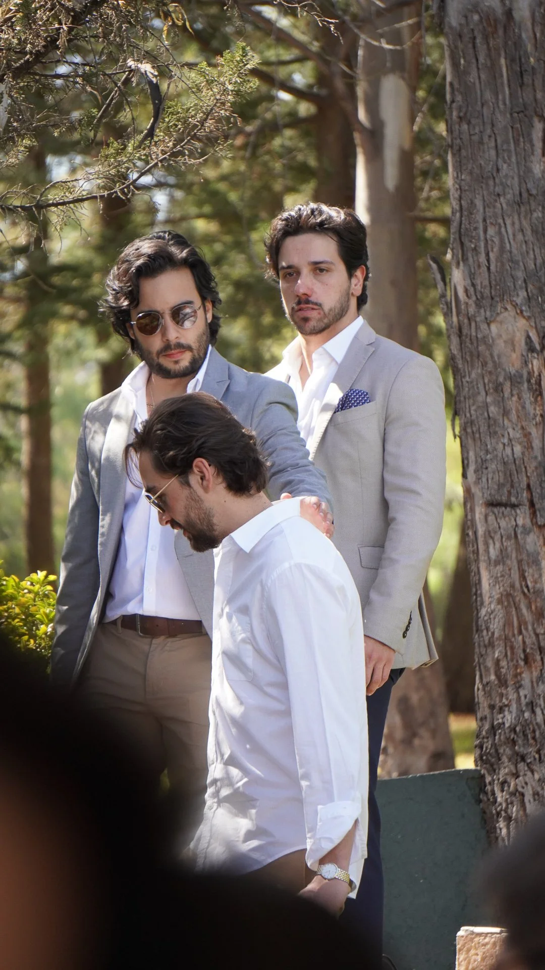 Cuatro hombres con vestimenta formal en un parque rodeados de árboles.