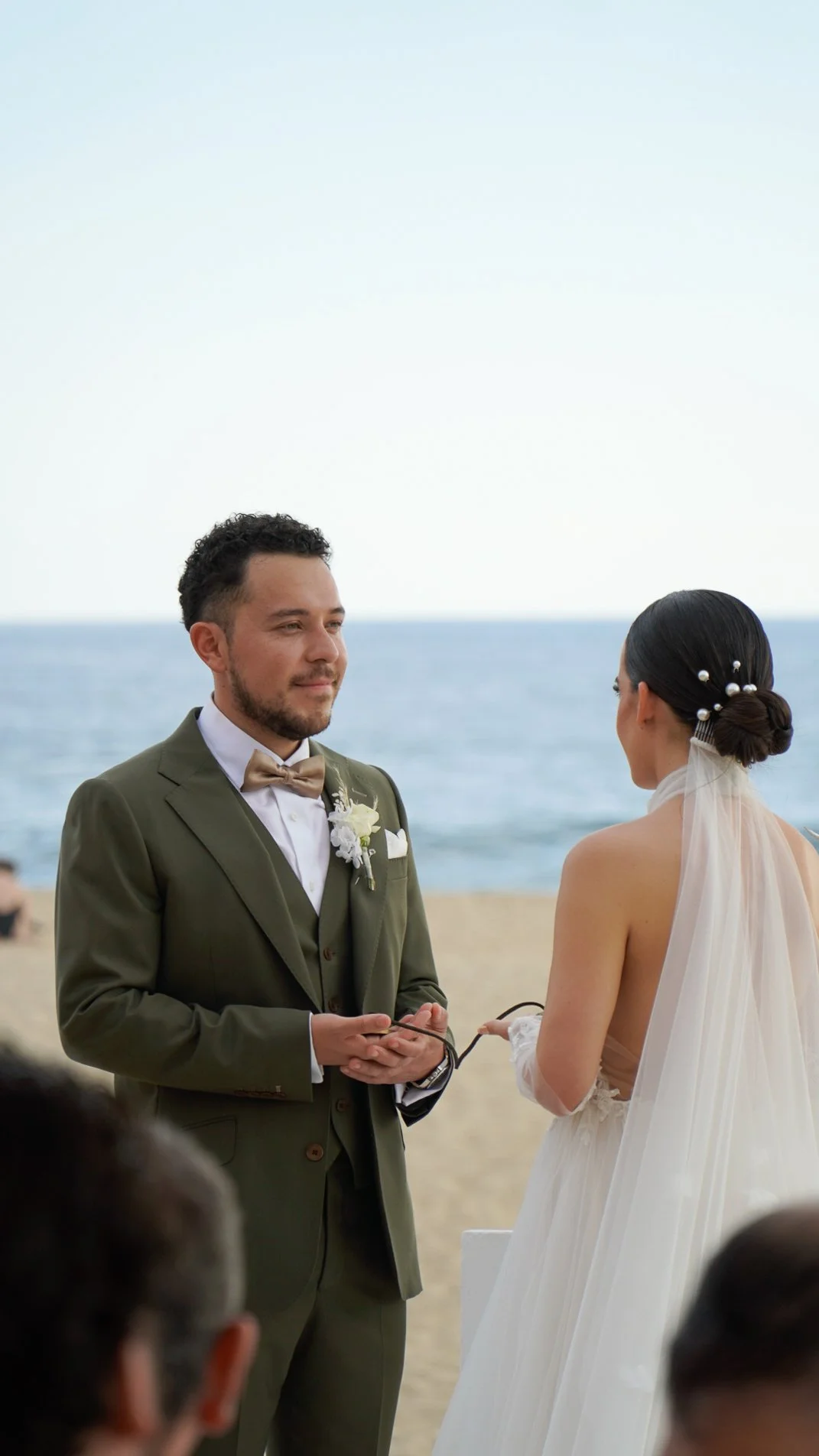 Pareja de novios intercambiando votos en una ceremonia de boda en la playa, con el mar de fondo.