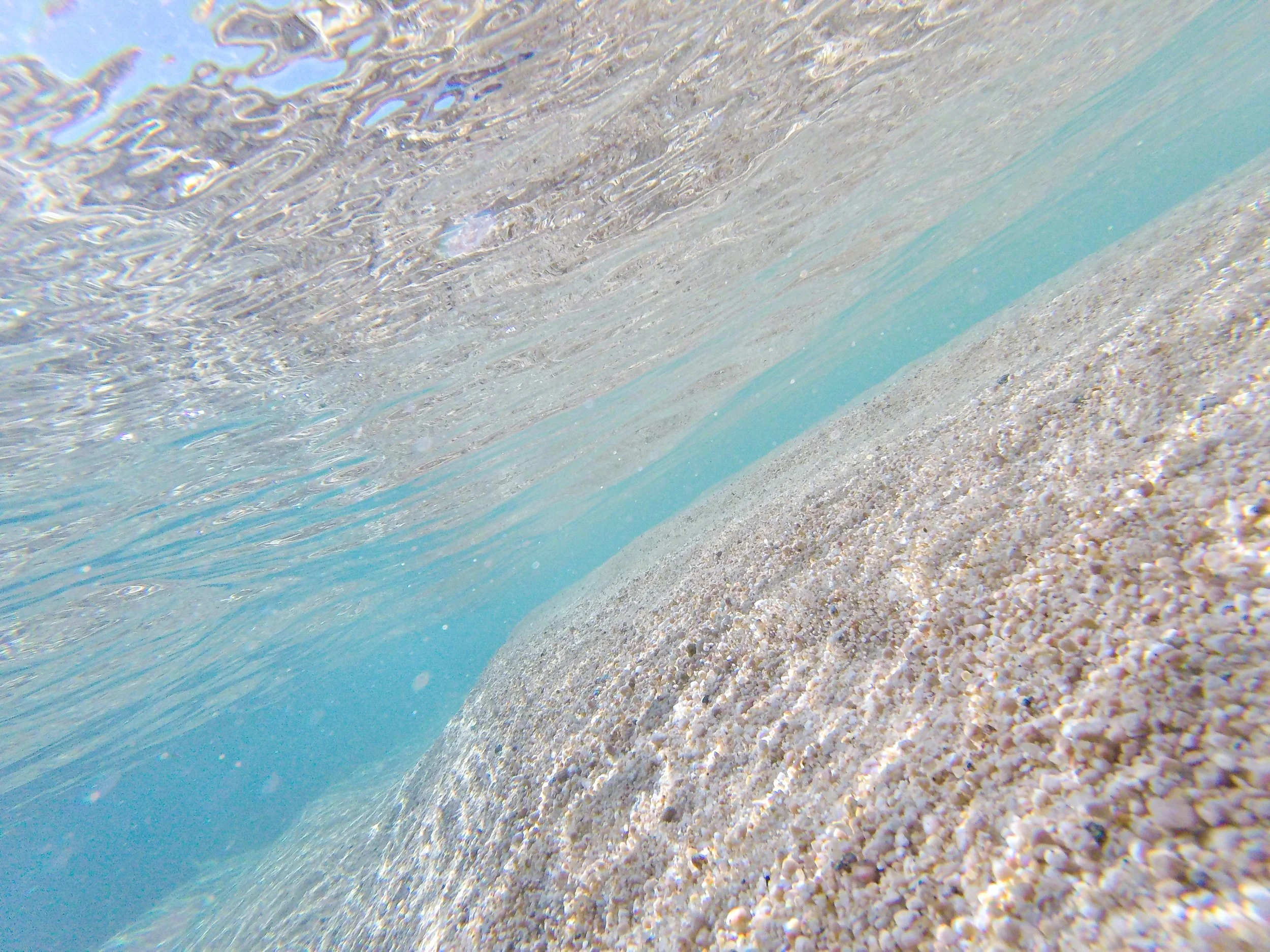 Vista submarina de arena y agua cristalina, con la superficie del agua visible en la parte superior.