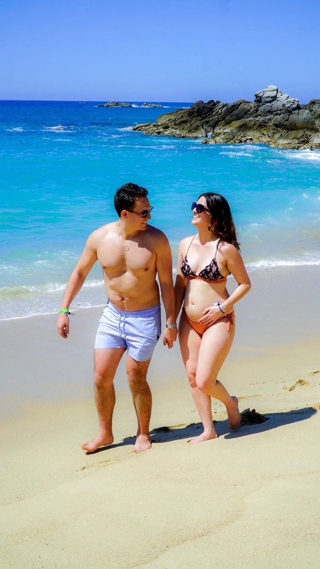 Pareja caminando por la playa con el mar azul de fondo