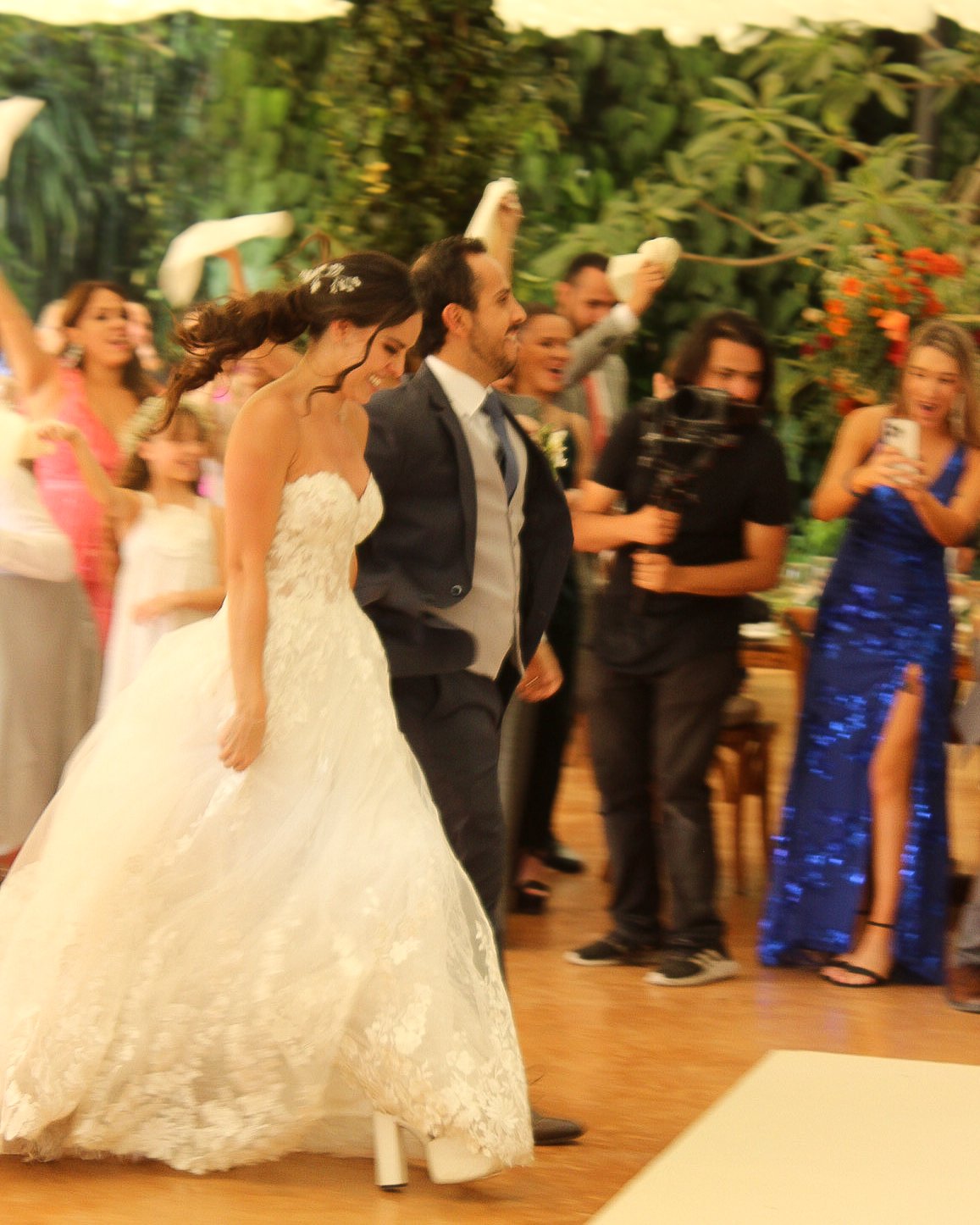 Pareja de recién casados caminando entre invitados en una celebración de boda con decoración natural y festiva.