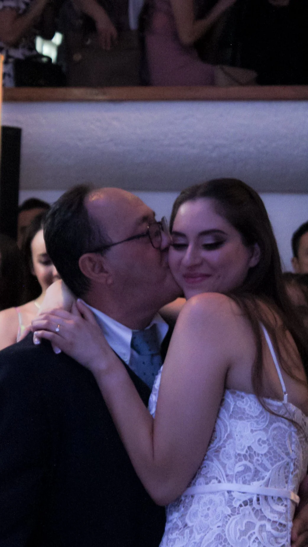 Un hombre besando a una mujer en un evento o fiesta con varias personas en el fondo.