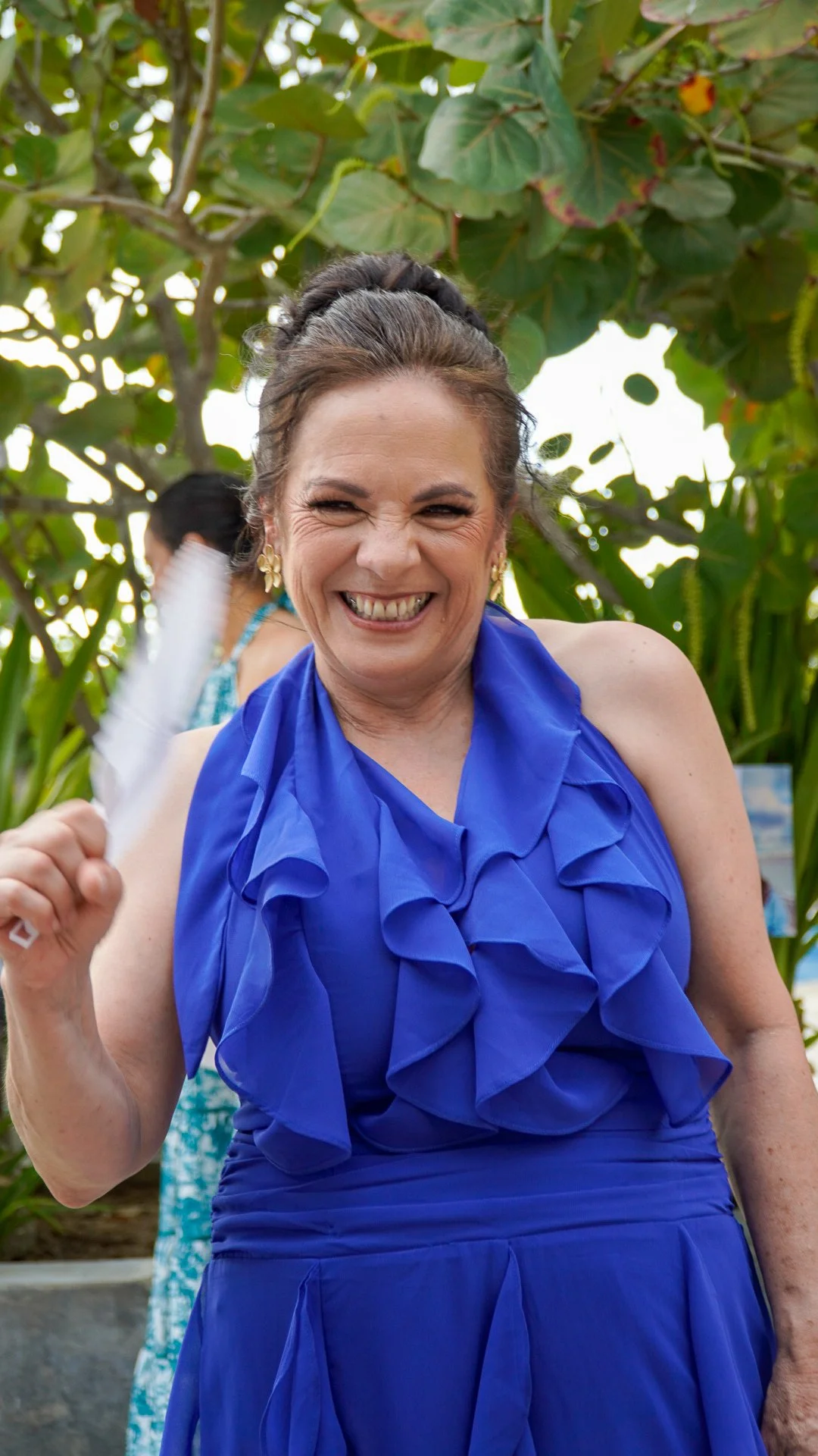 Mujer sonriendo con vestido azul en un entorno de vegetación.