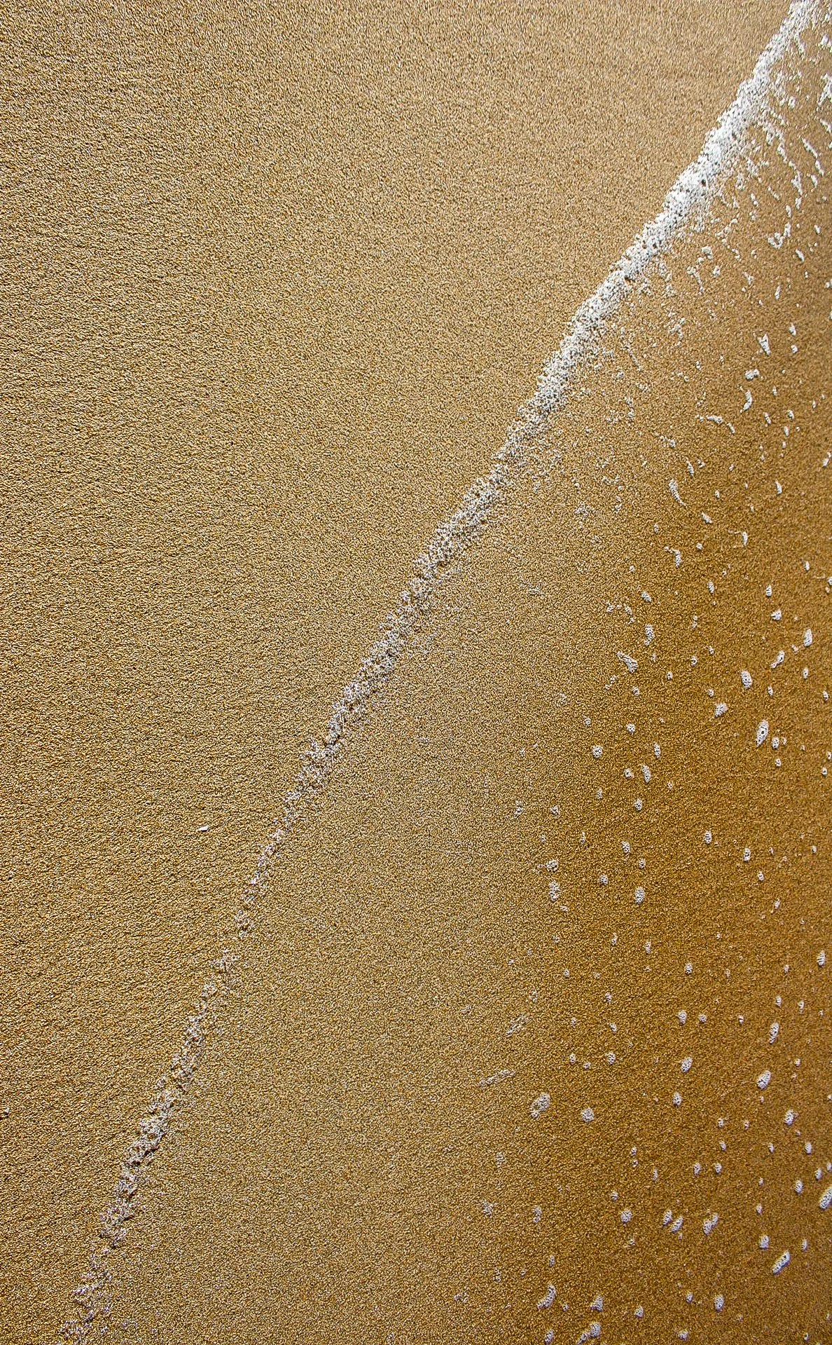 Vista de la arena de la playa y la orilla con olas llegando.