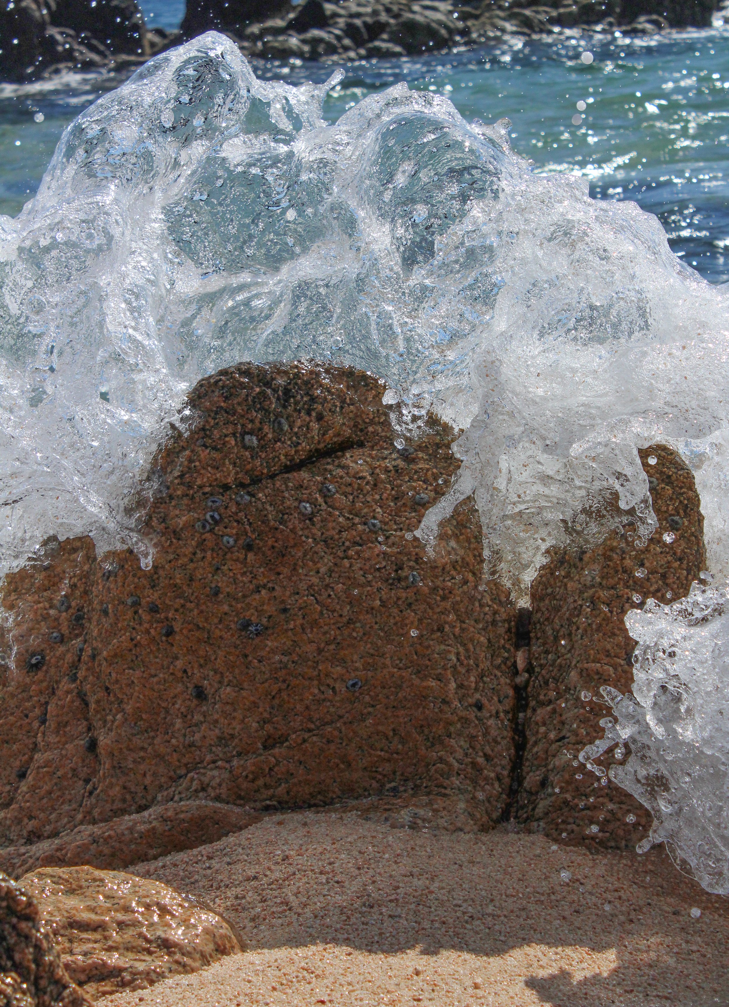 Olas del mar rompiendo sobre rocas con arena en la playa.