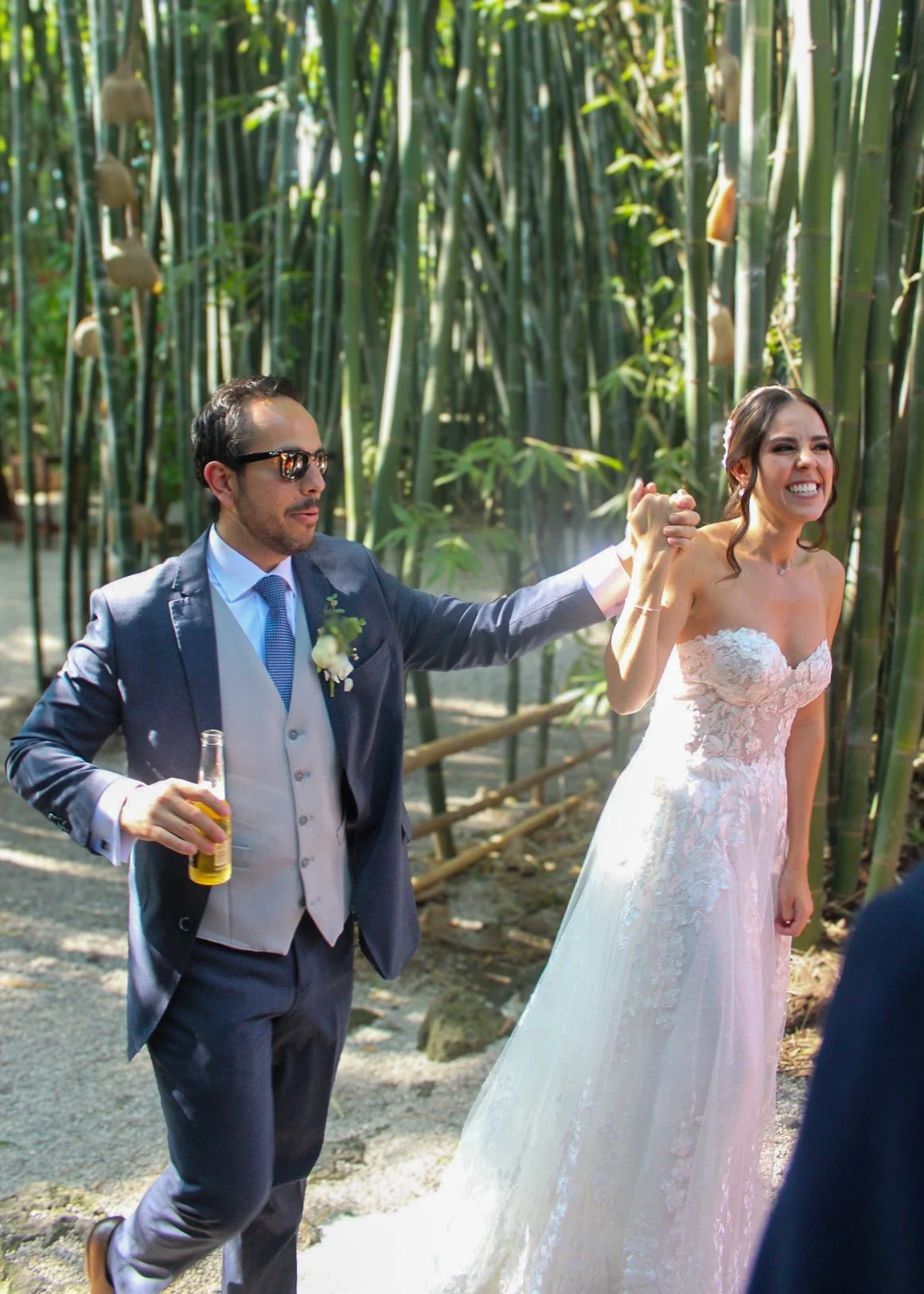 Una pareja de boda en un entorno natural, con el novio sosteniendo una bebida y fajando a la novia, que está sonriendo con entusiasmo.
