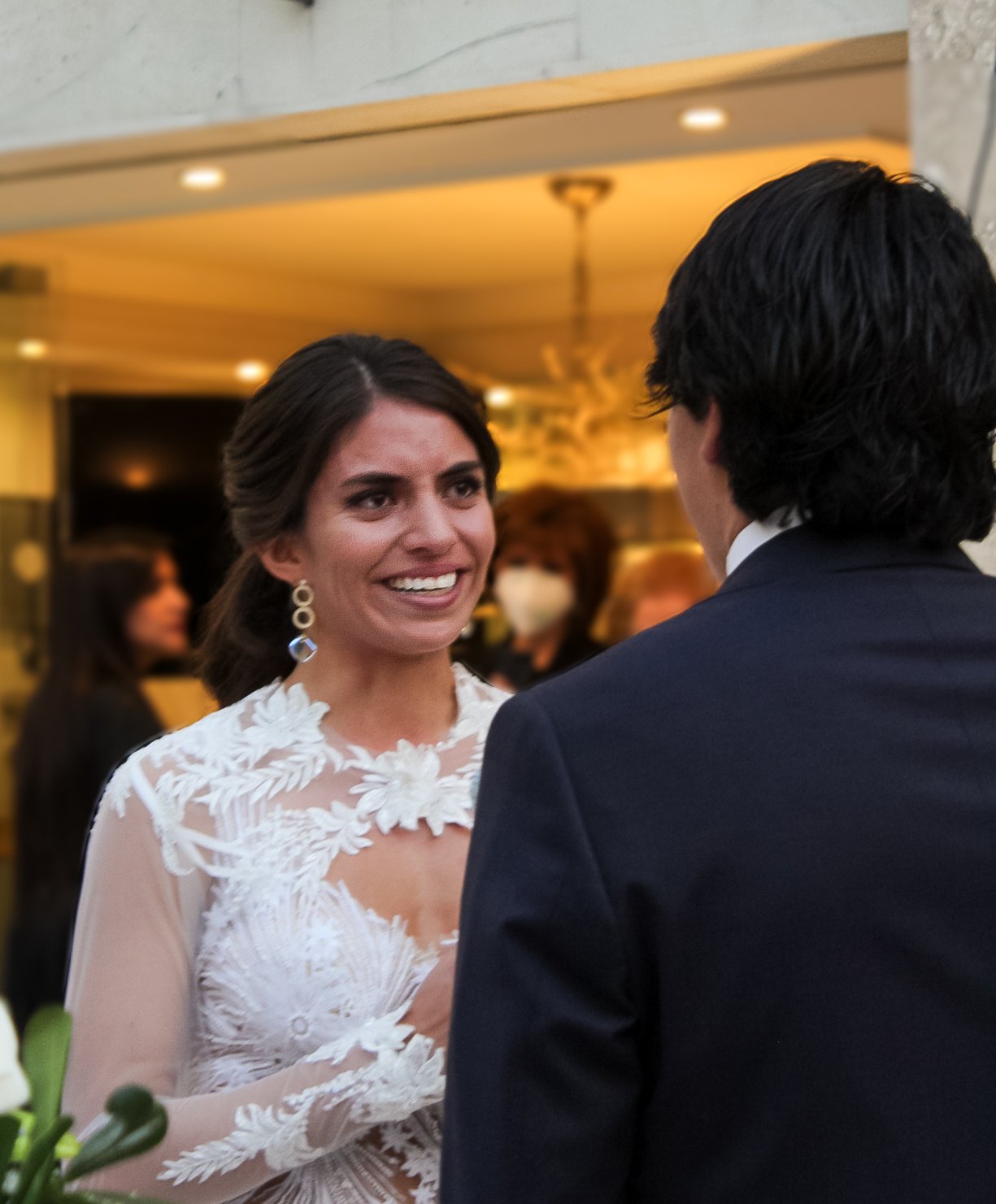 Una mujer con vestido de novia y un hombre en un traje oscuro en una boda, ambos conversando.