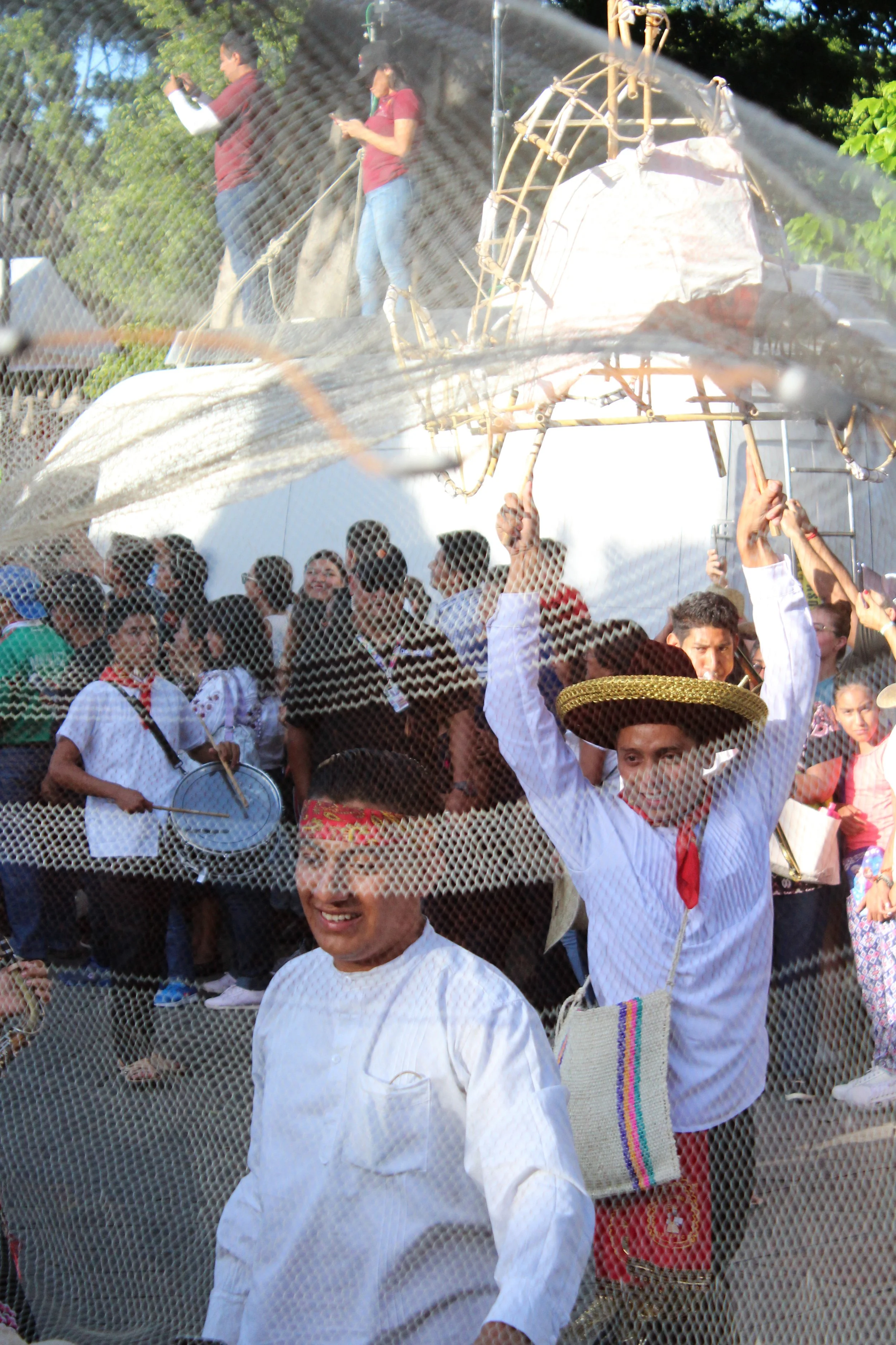 Personas participando en una celebración con disfraces típicos, algunos llevan sombreros grandes y otros con instrumentos musicales, en un evento al aire libre.