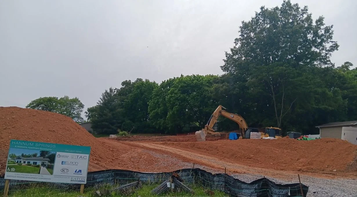 Multifamily new construction development with fresh soils and excavator and green trees