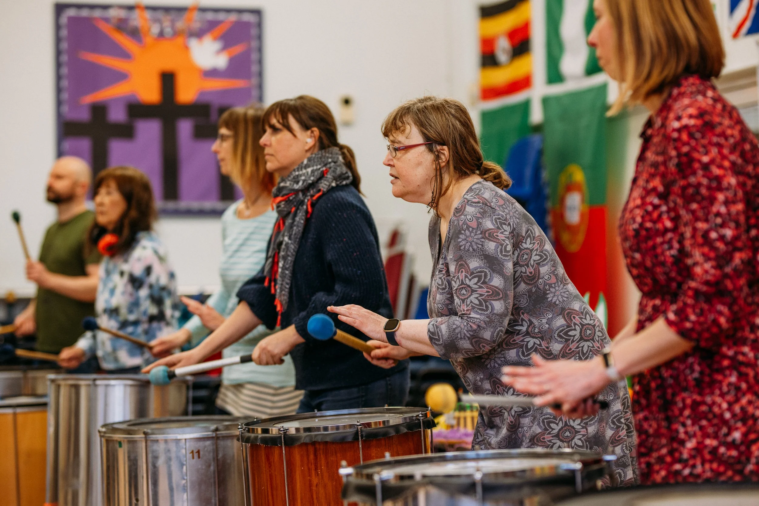 Group of people standing in a row playing steel drums in a church or community center with religious and national flags in the background