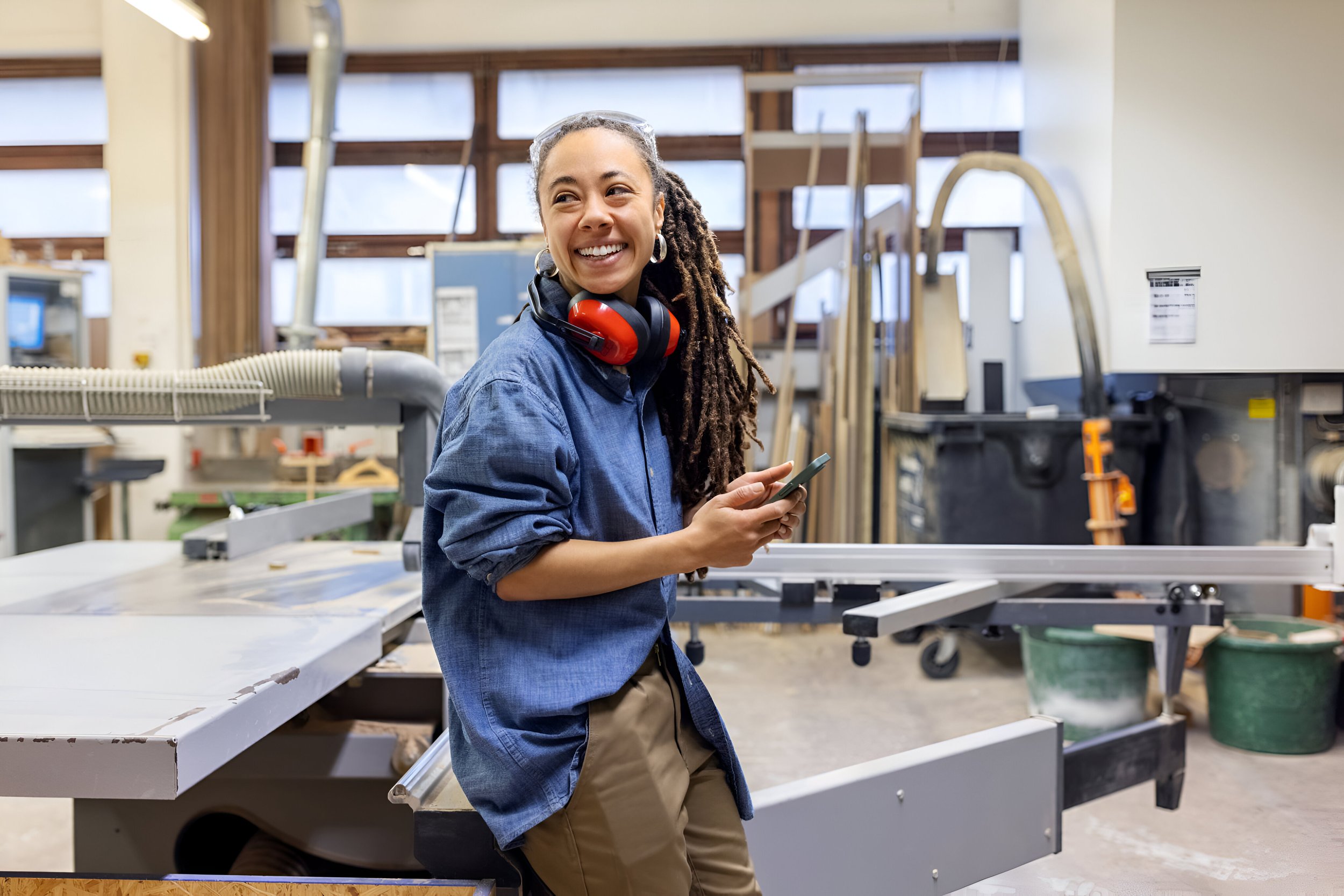 woman-holding-cell-phone-looking-away-smiling-carpentry-workshop.jpg