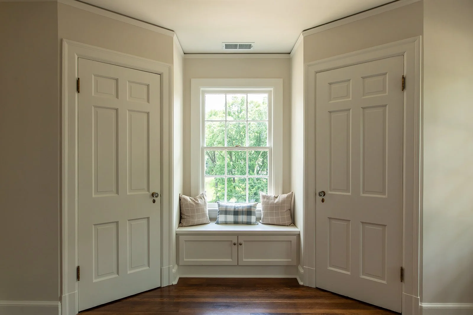 Built-in window seat tucked between two closet doors with treetop views