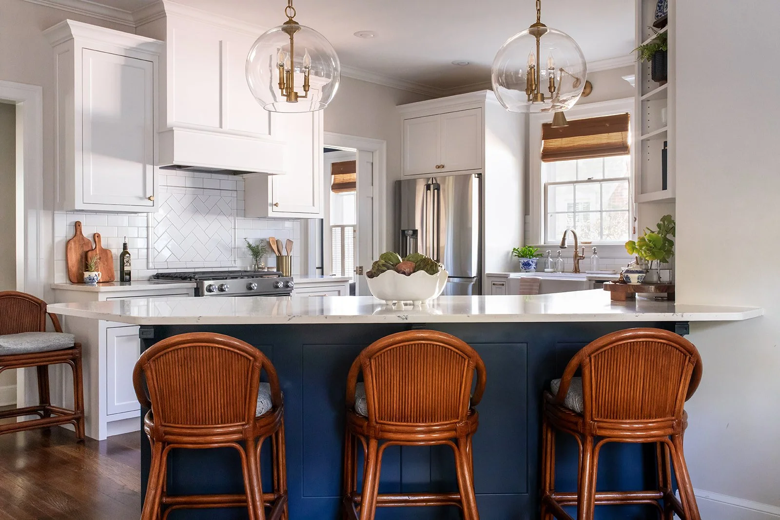 Navy kitchen island with white cabinets, brass globe pendants, and rattan barstools in a whole-home remodel