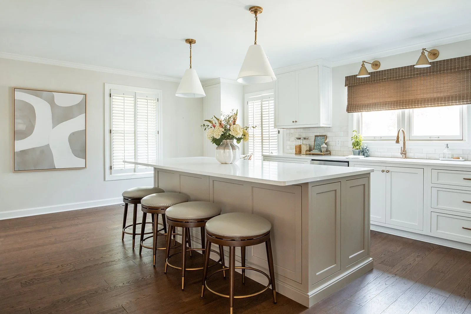 White kitchen island with woven stools, brass pendants, and abstract art