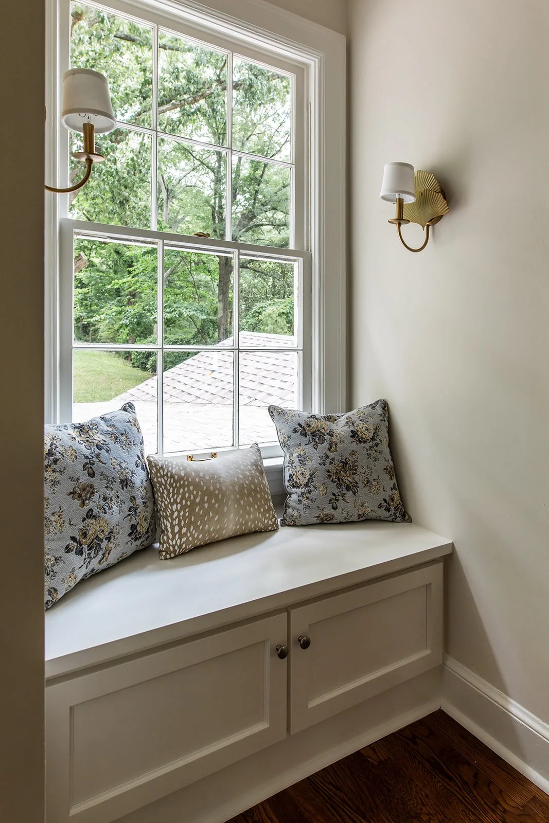  Window seat with a painted cabinet base, blue floral pillows and brass sconces in a 1942 Colonial. 