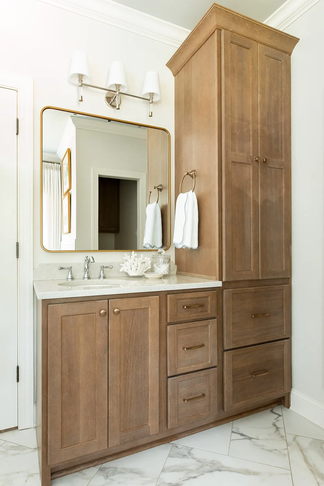 Wood double vanity with a linen tower, brass mirrors, and marble counters