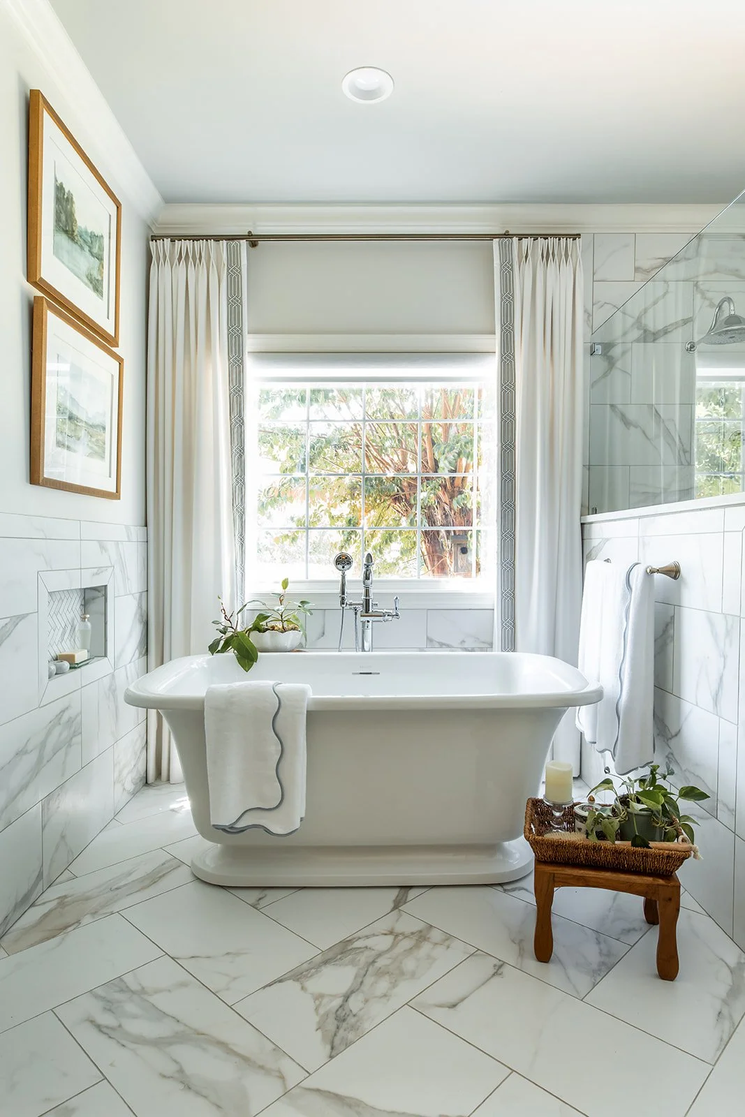 Cast stone soaking tub beneath a window with tree views and marble-look floors