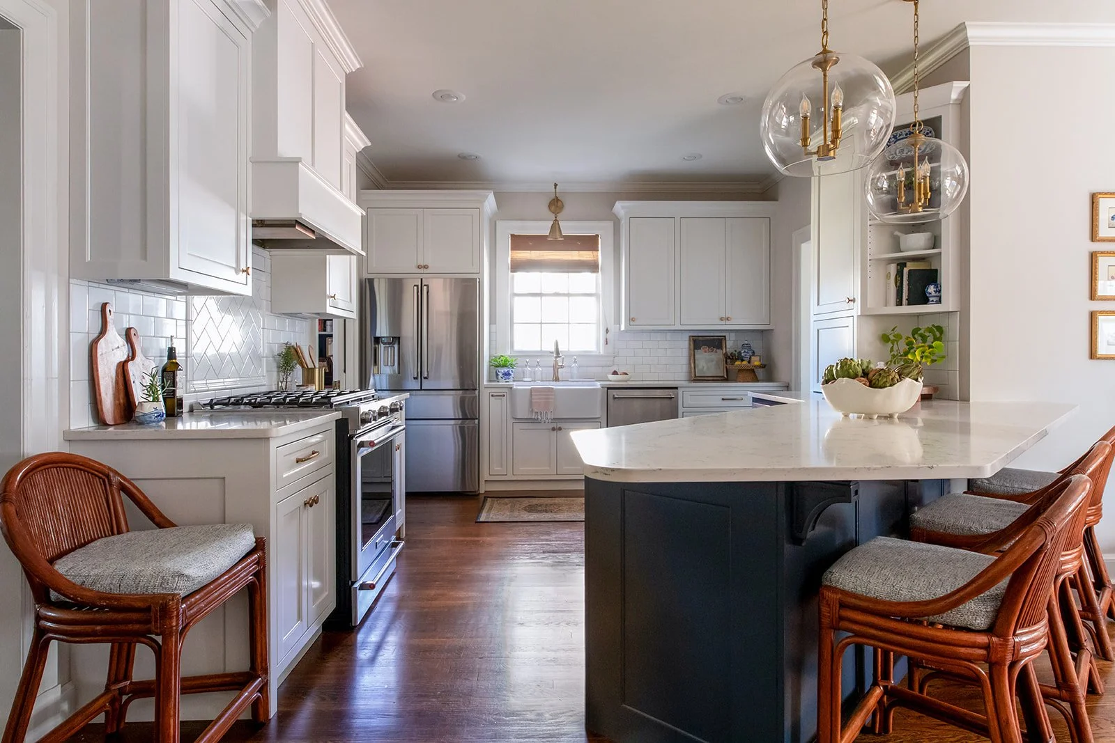 White kitchen with a navy island, brass pendants, and hardwood floors open to the dining area
