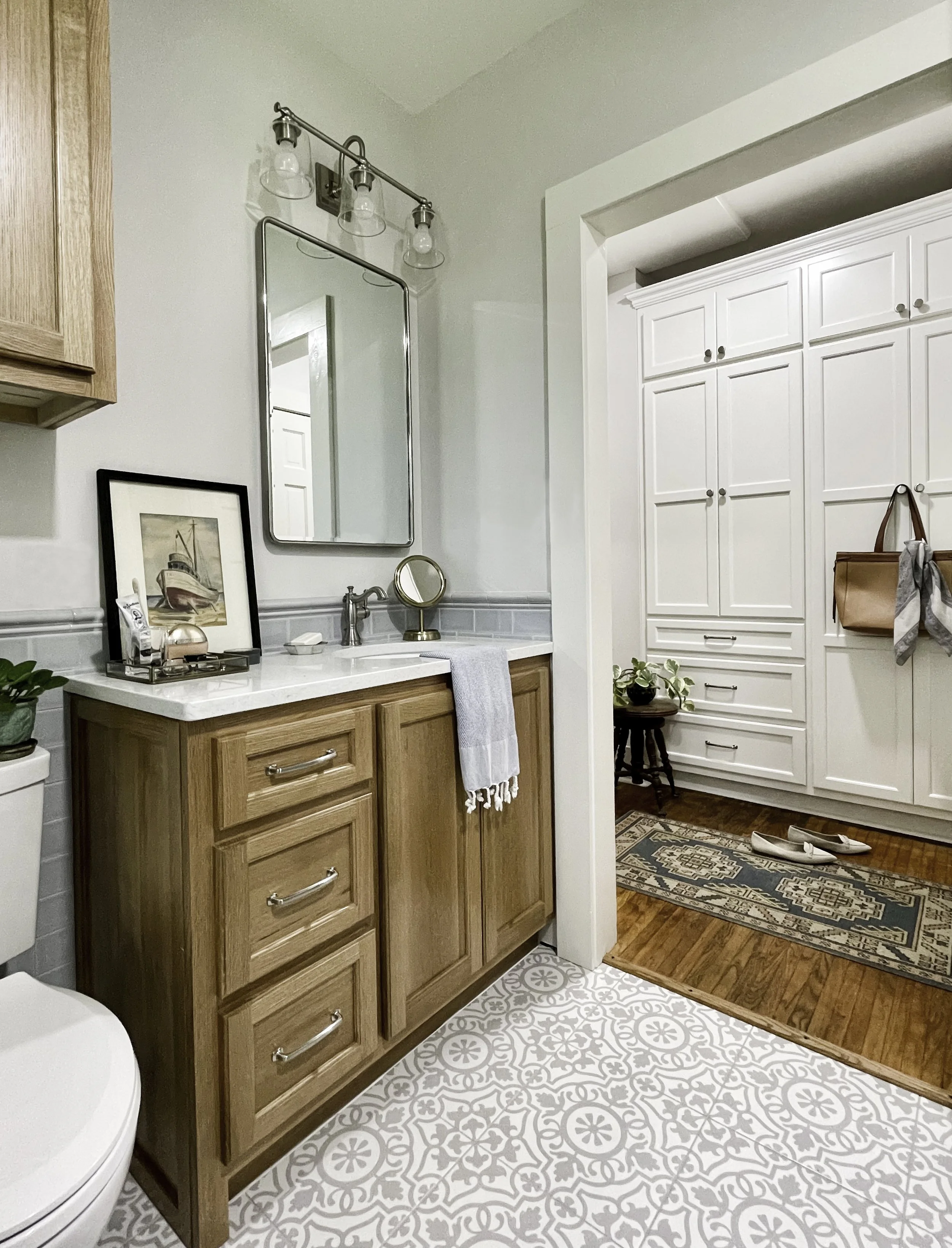 Wood vanity with a mirror, chrome sconces, and marble counter with a view to the closet