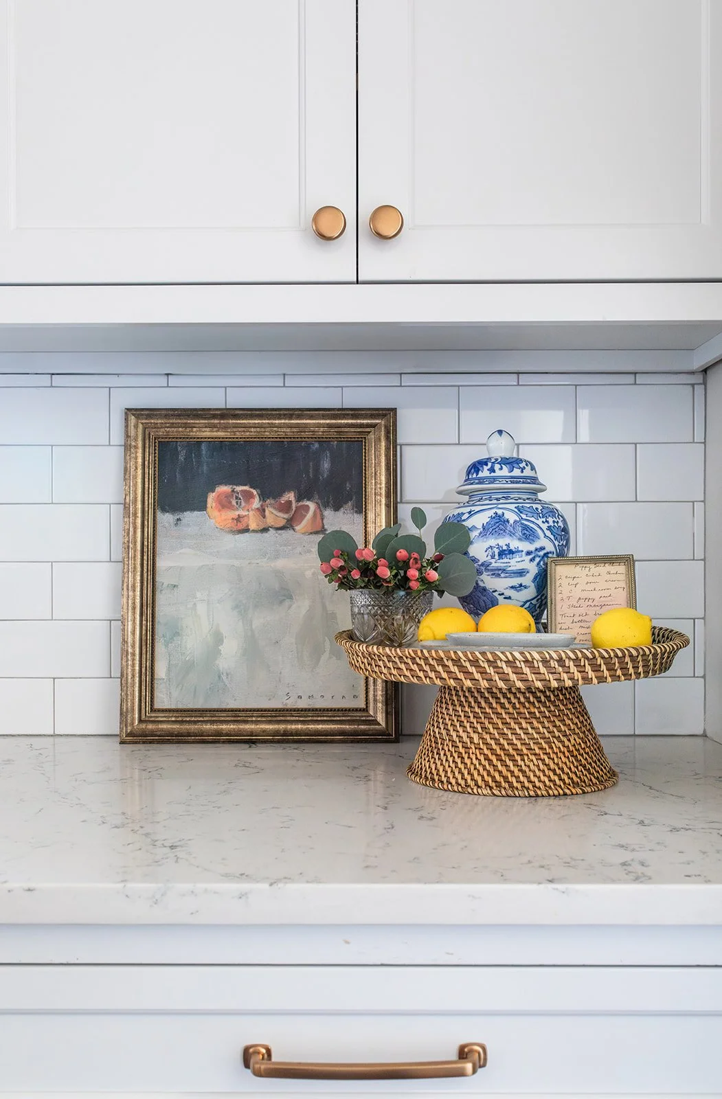 Kitchen backsplash vignette with framed art, a ginger jar, and lemons on quartz