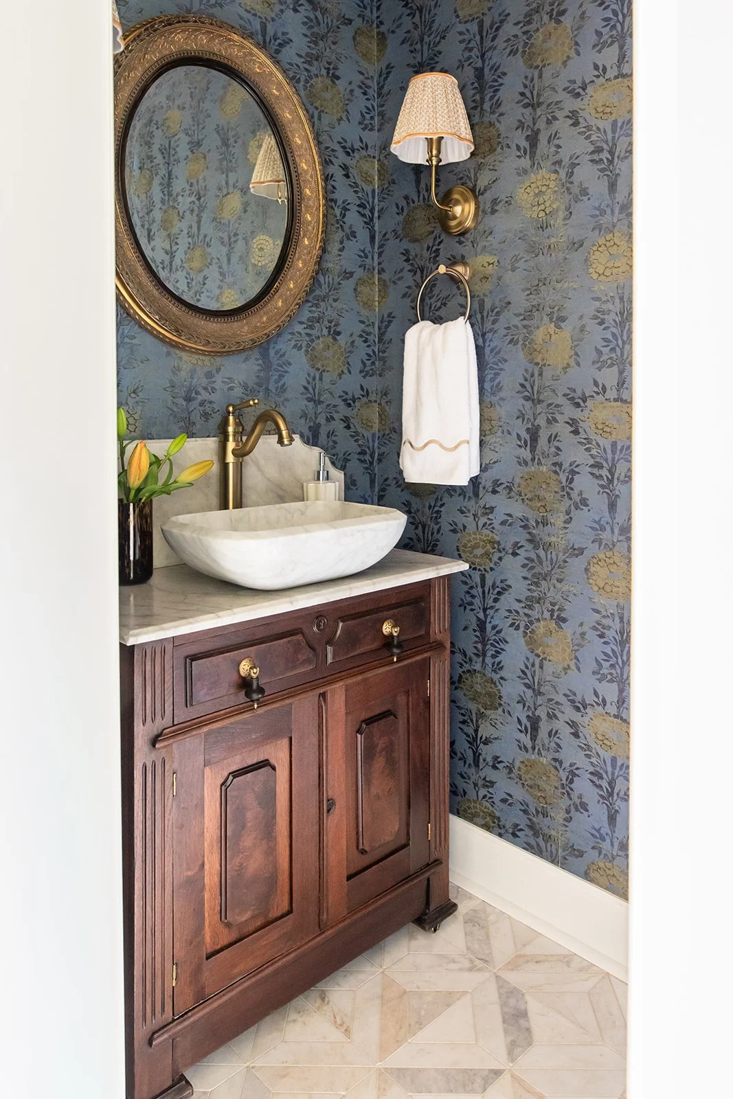 Powder room with dramatic botanical wallpaper and an antique wood vanity