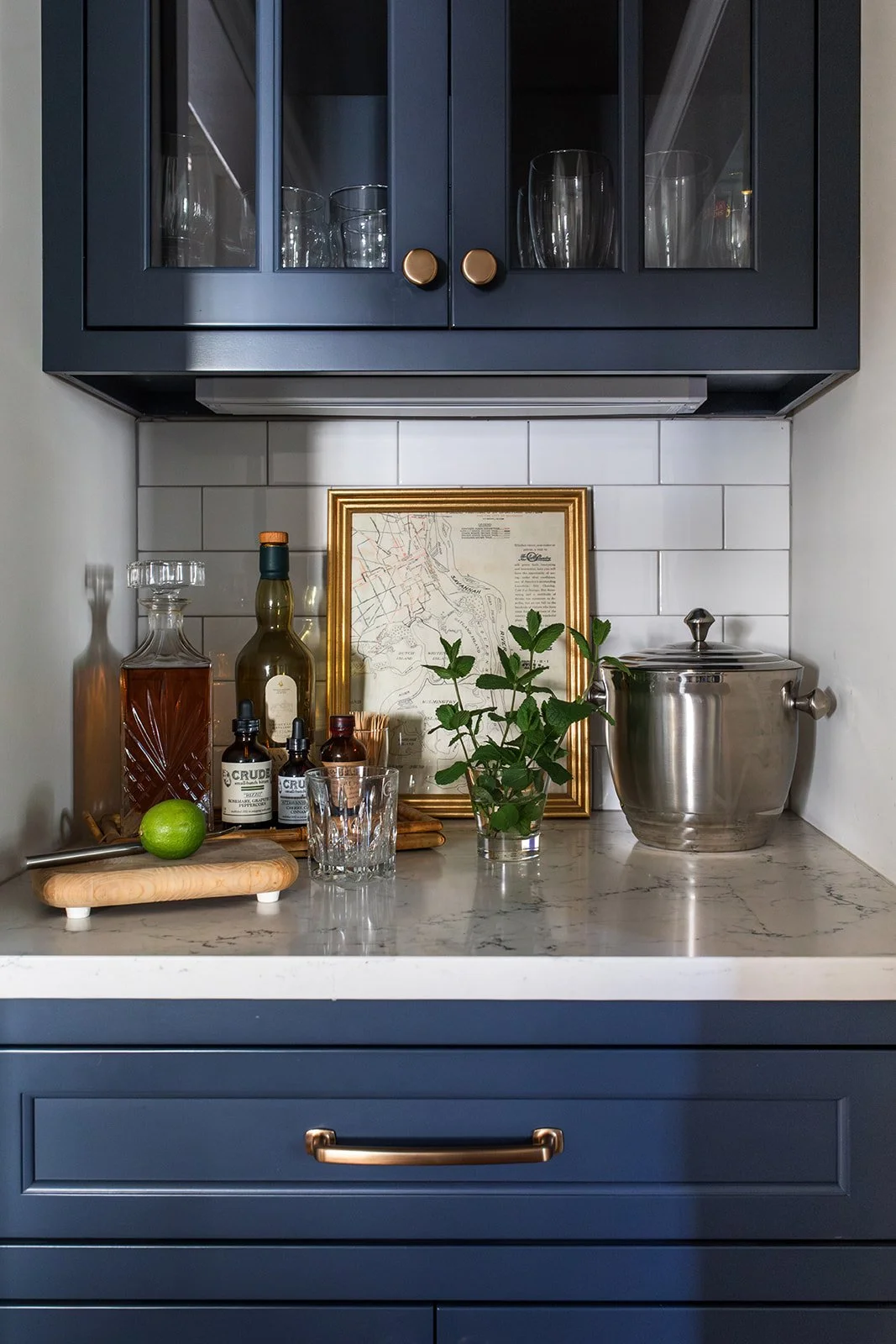 Navy bar counter styled with framed art, bottles, and greenery on quartz