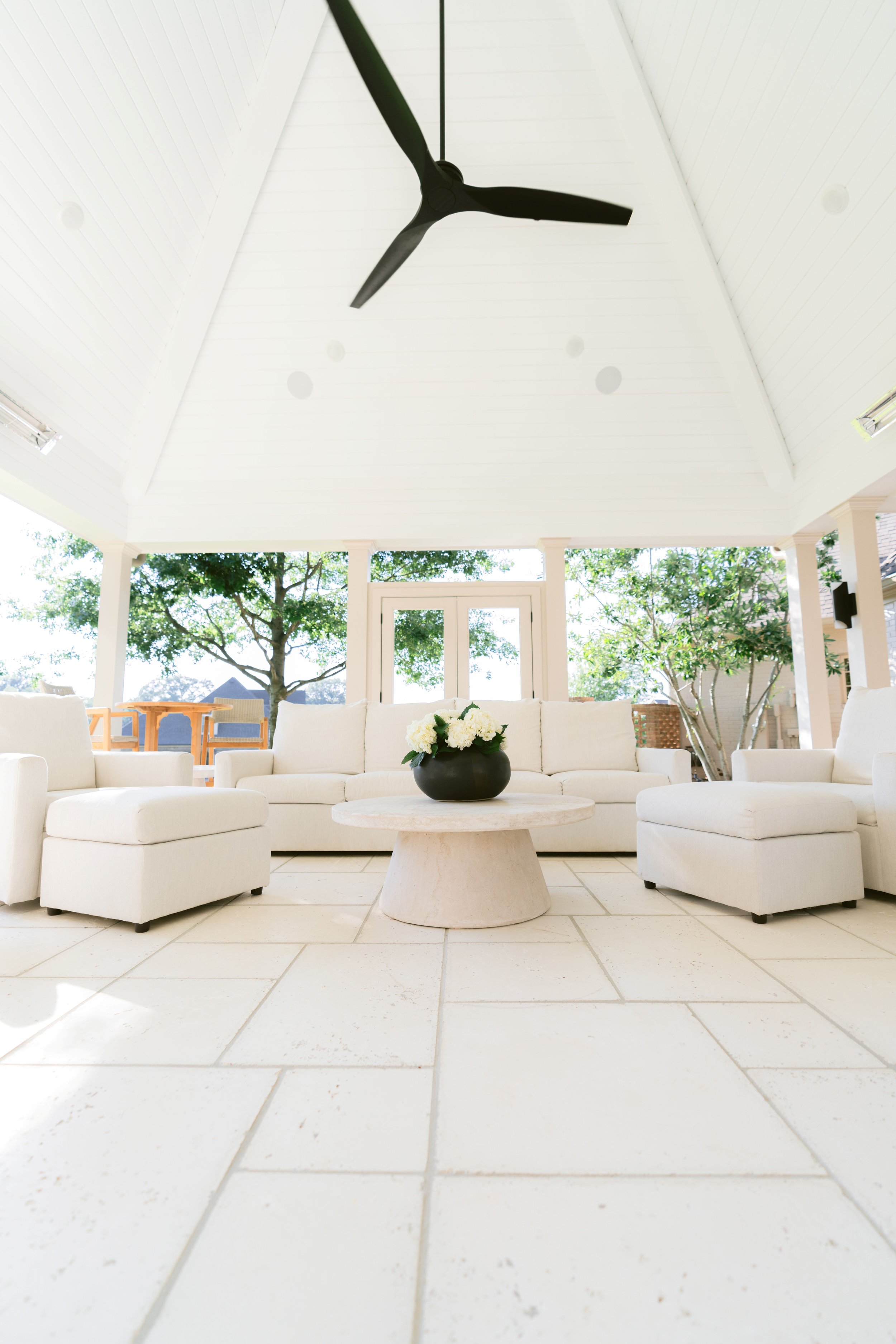 Covered outdoor living area with a vaulted ceiling, modern fan, and white lounge seating